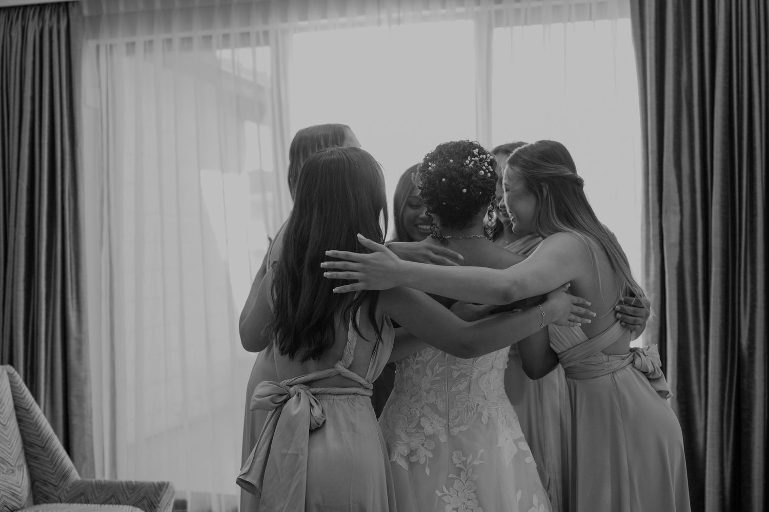 Black and white photo of a bride sharing an emotional group hug with her bridesmaids.