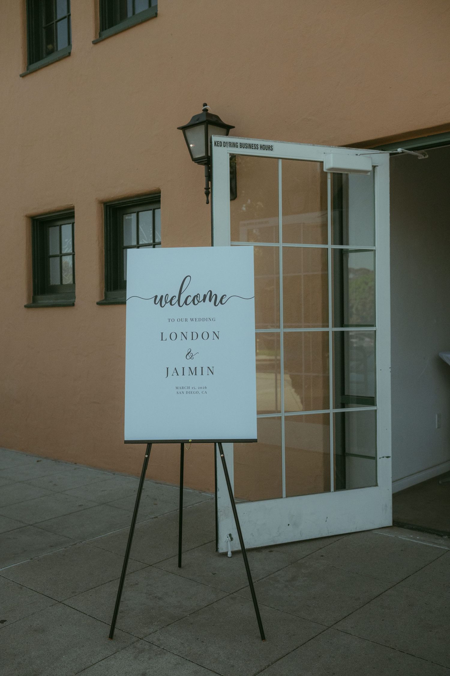 Elegant wedding welcome sign on easel for London and Jaimin outside a venue with warm terracotta walls.