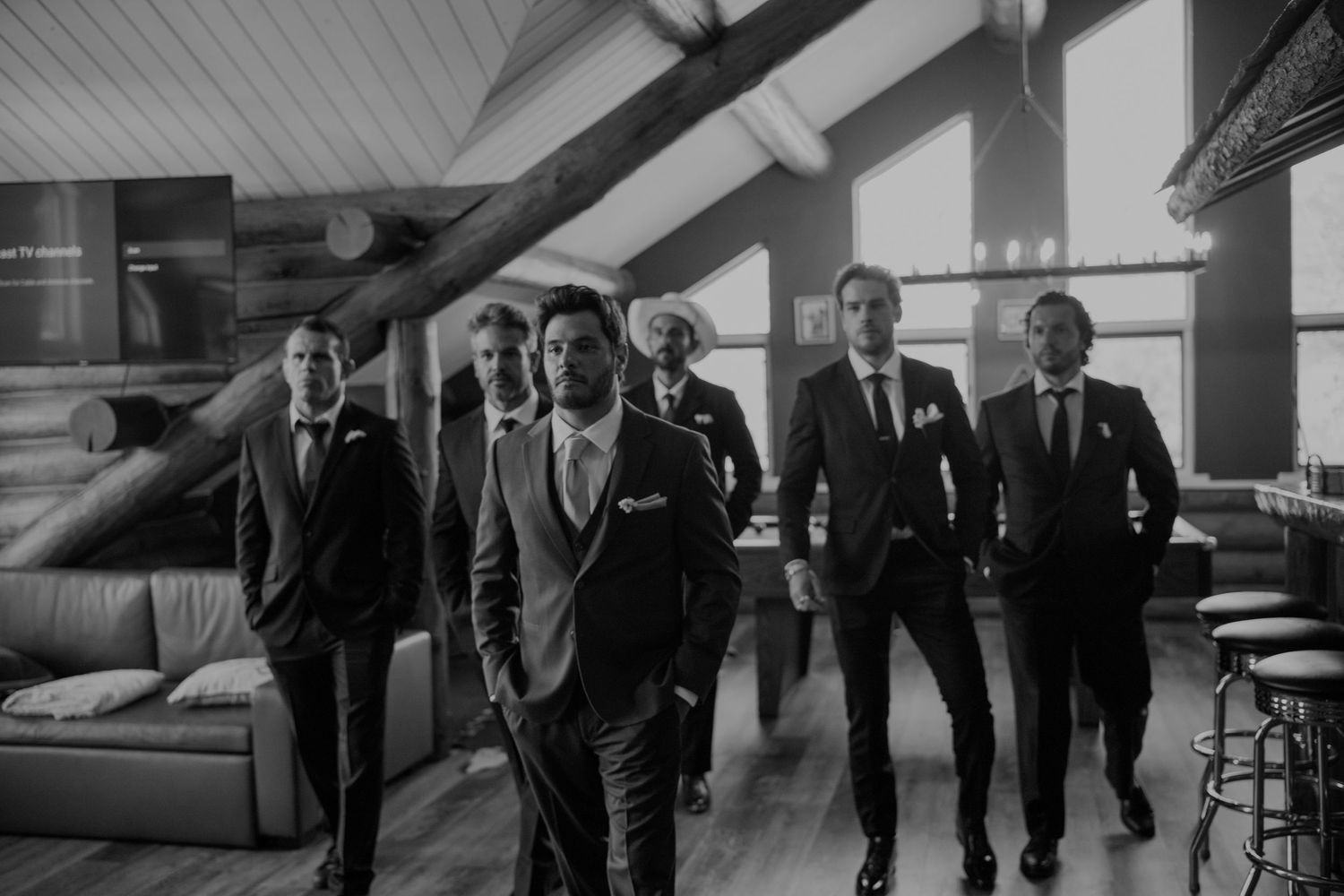 Groomsmen in dark suits walking together through a rustic wedding venue in black and white photo.