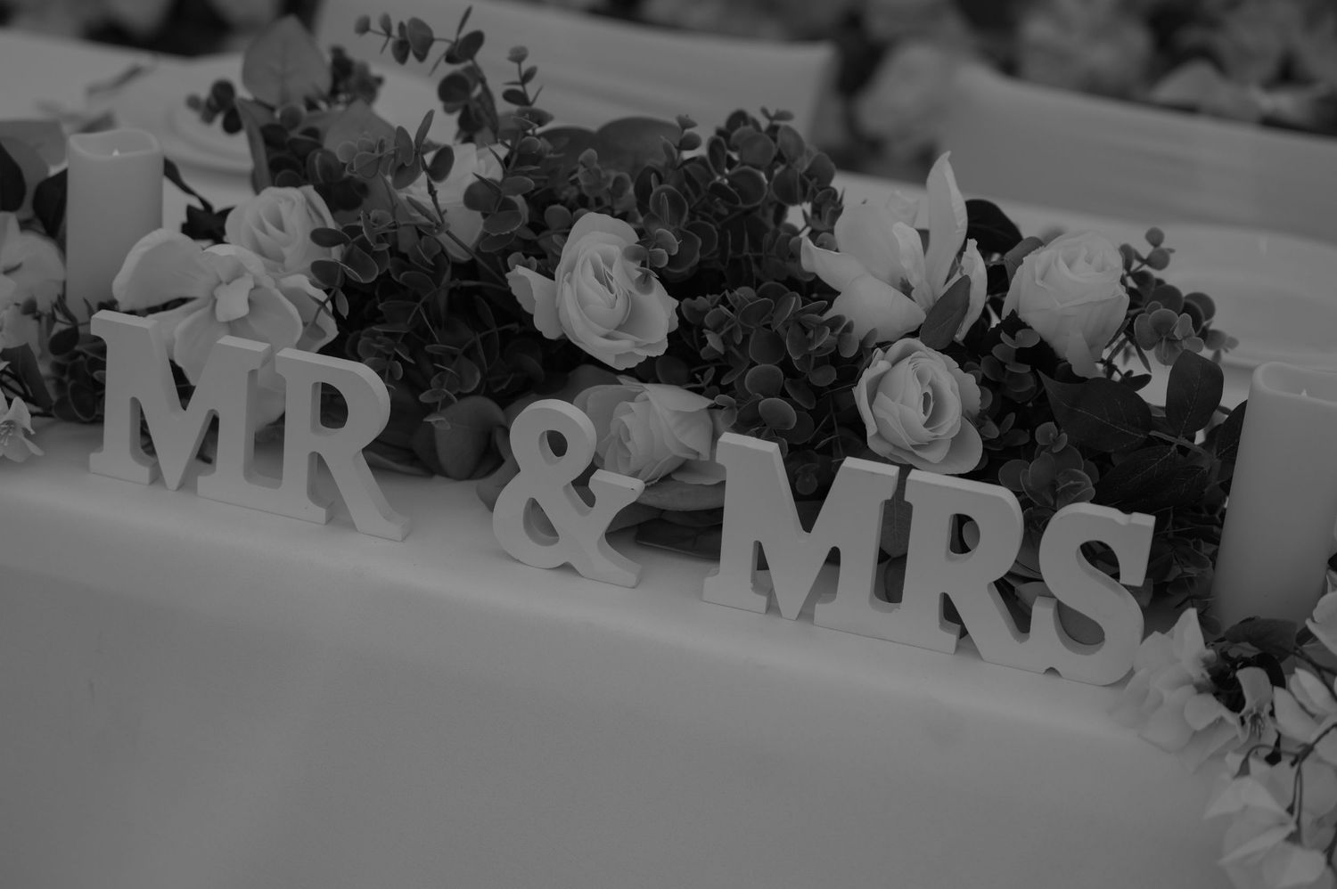 Black and white photo of Mr & Mrs wooden letters surrounded by roses at wedding reception.