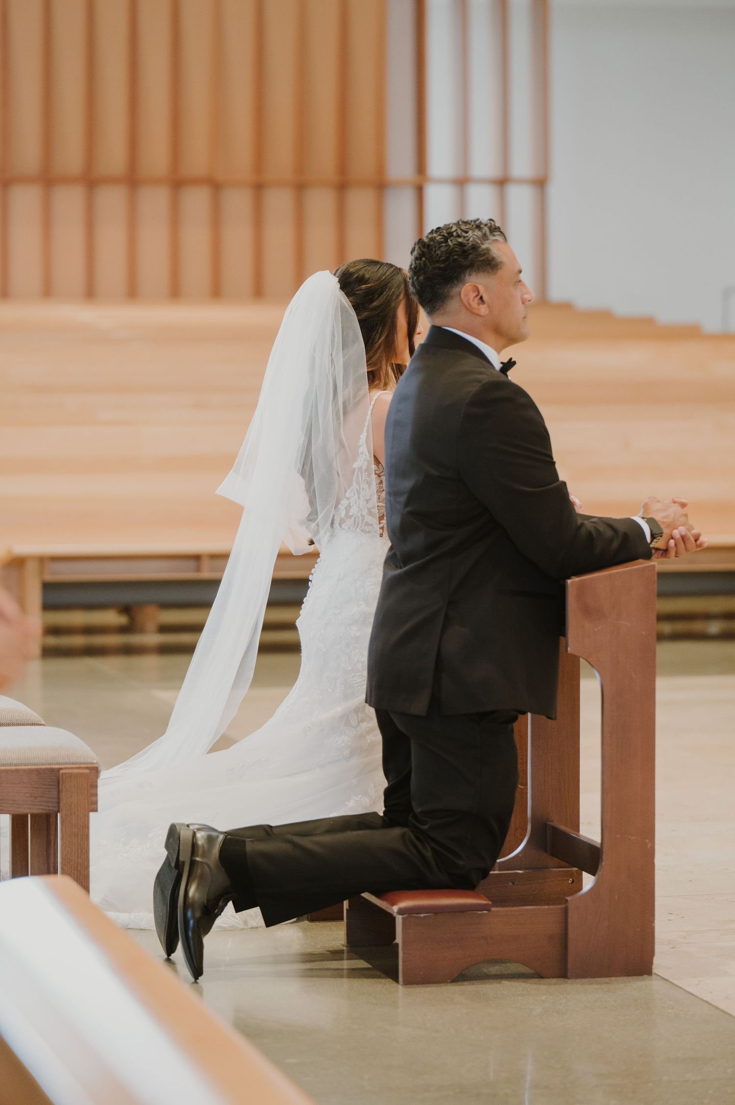 Bride and groom kneeling at the altar in prayer during their wedding ceremony in a modern church.