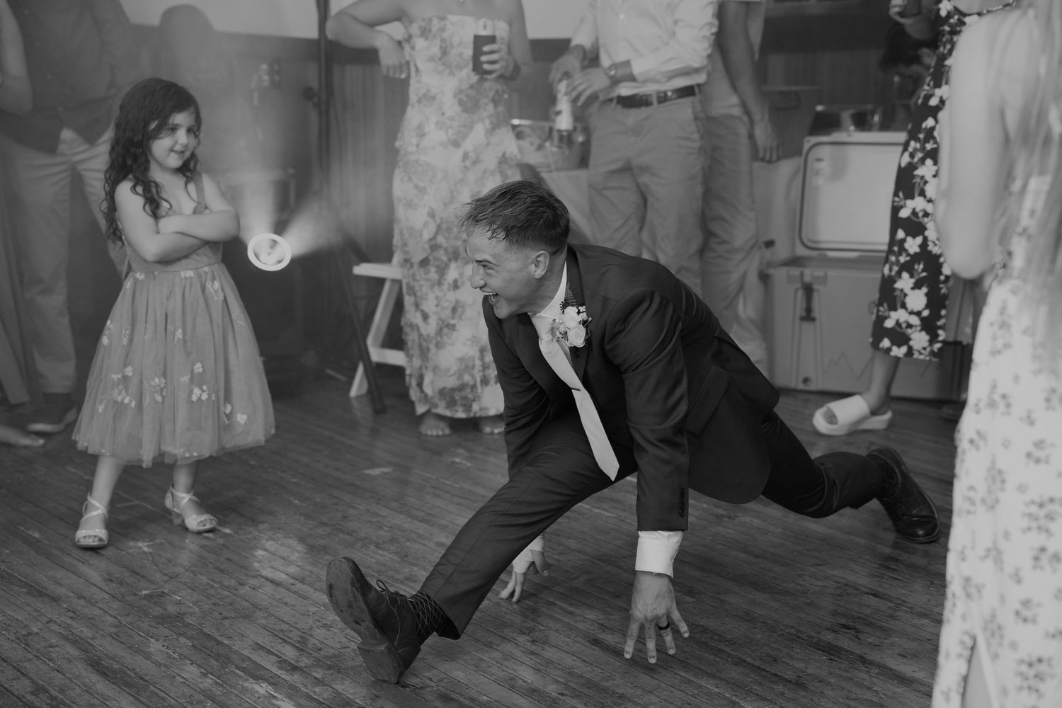 Black and white photo of wedding guests dancing energetically on wooden dance floor.