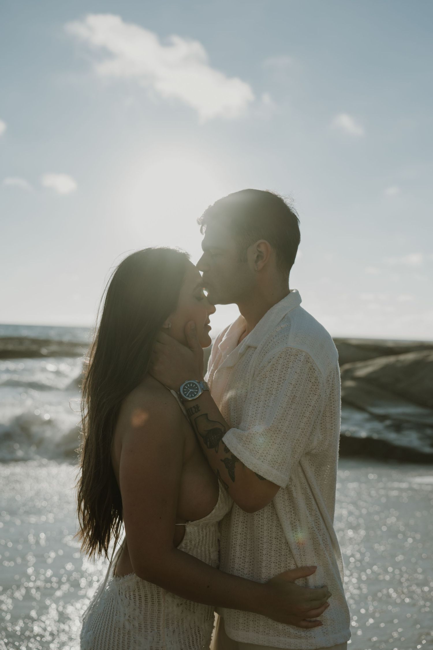 Silhouetted couple sharing an intimate moment against sparkling ocean waters.