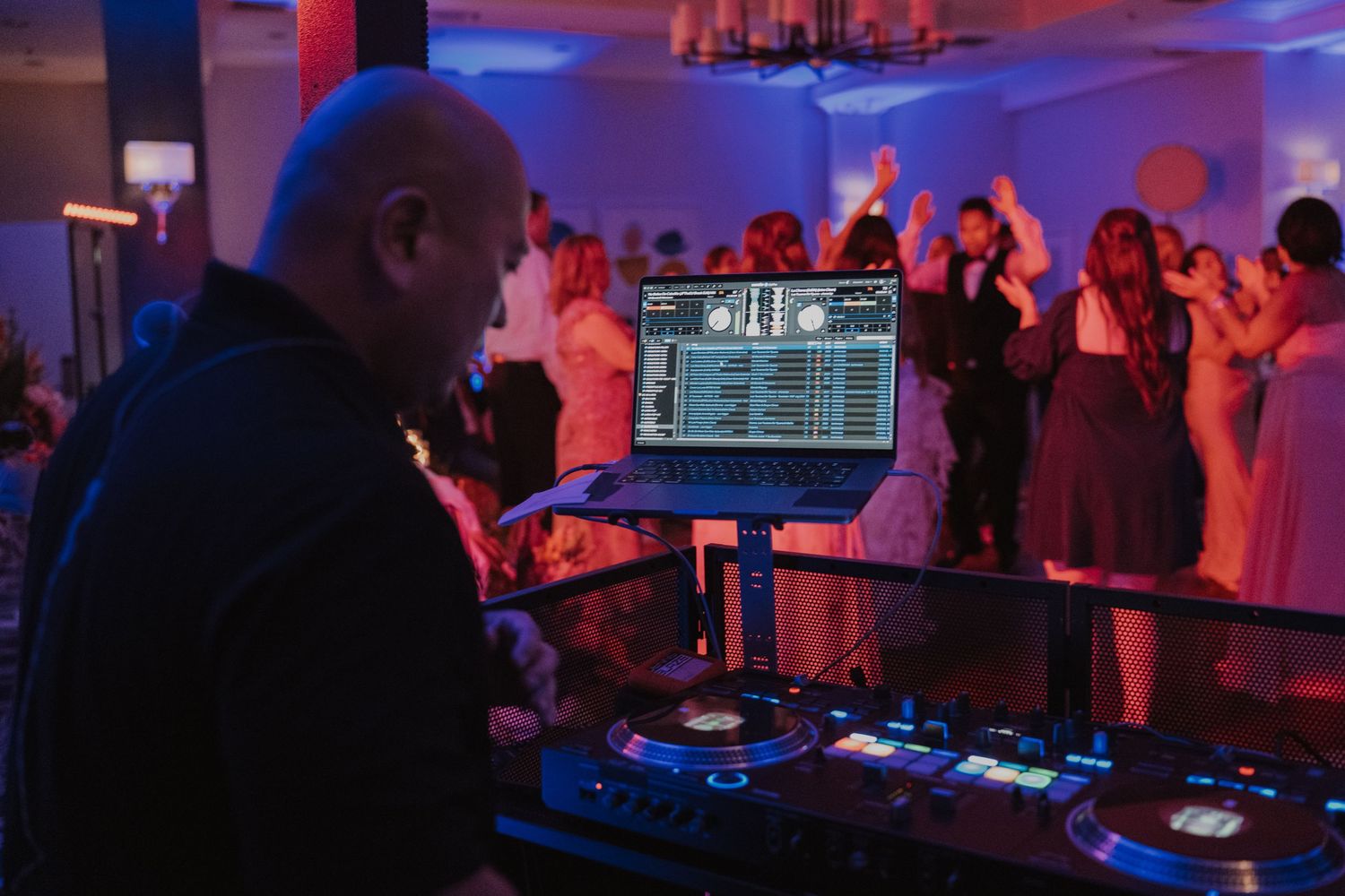 DJ equipment and dancing silhouettes illuminated by purple lighting at a wedding reception.