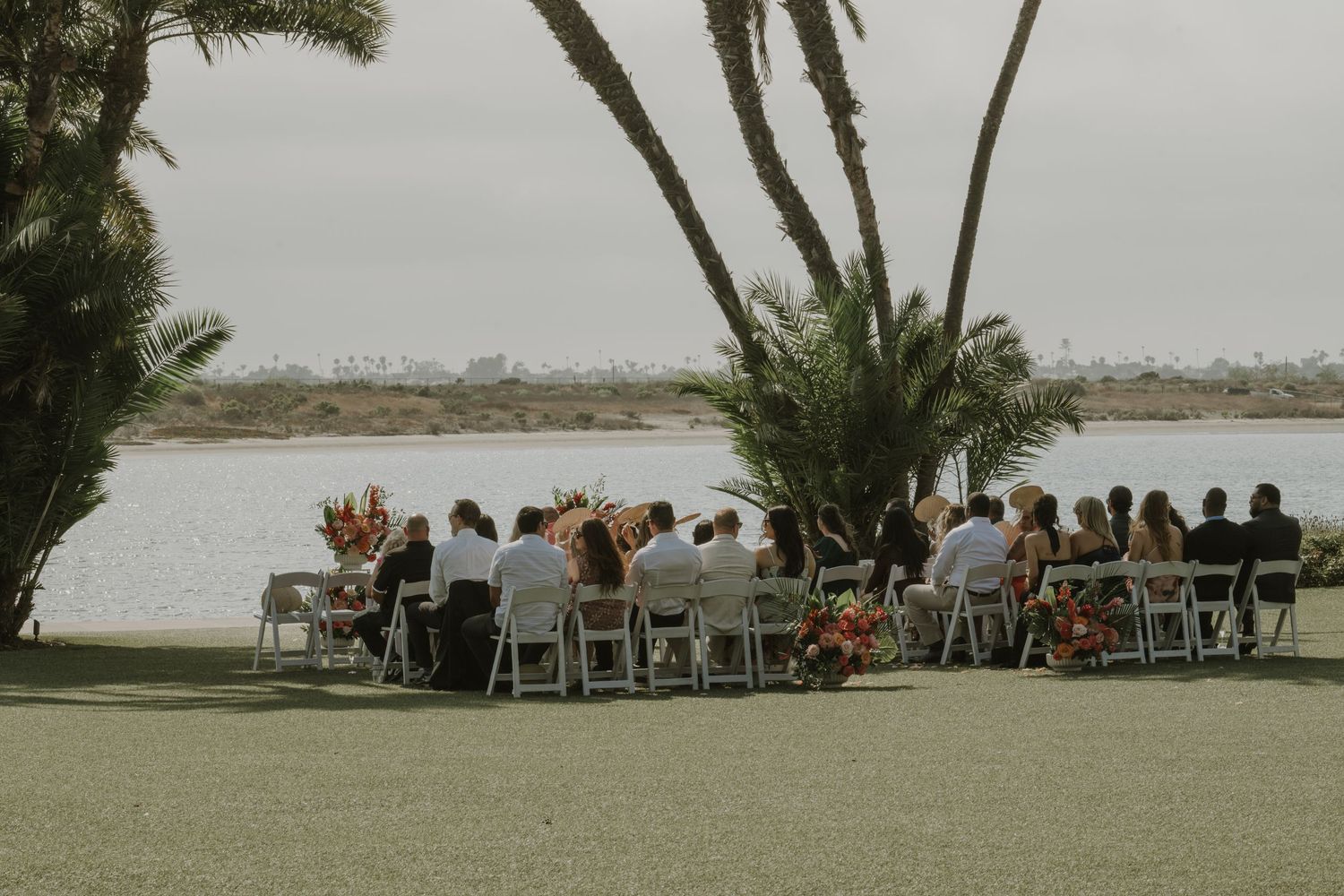 Waterfront wedding ceremony setup with white chairs and palm trees.