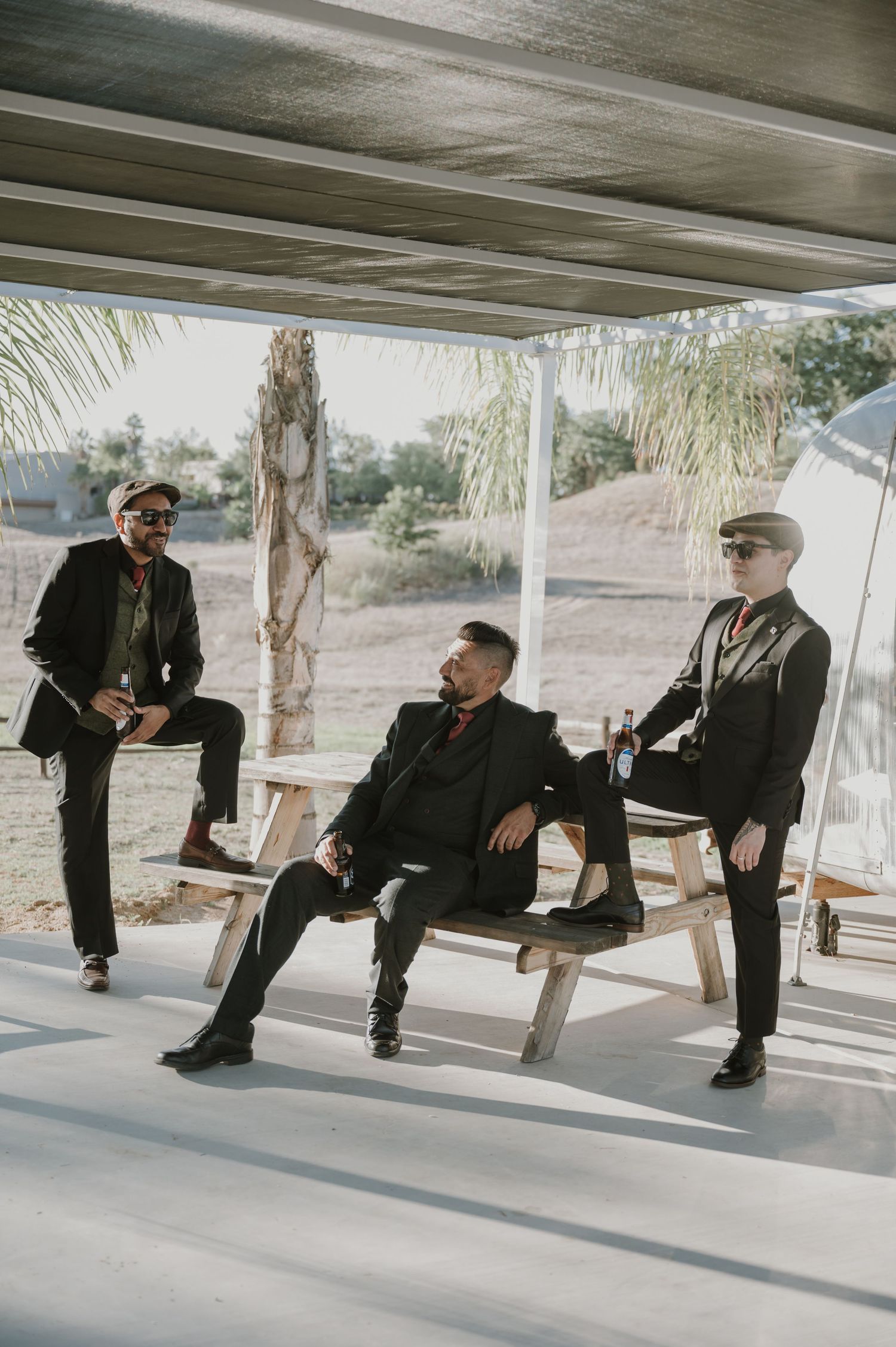 Multiple figures in dark suits seated on benches under a covered outdoor area.