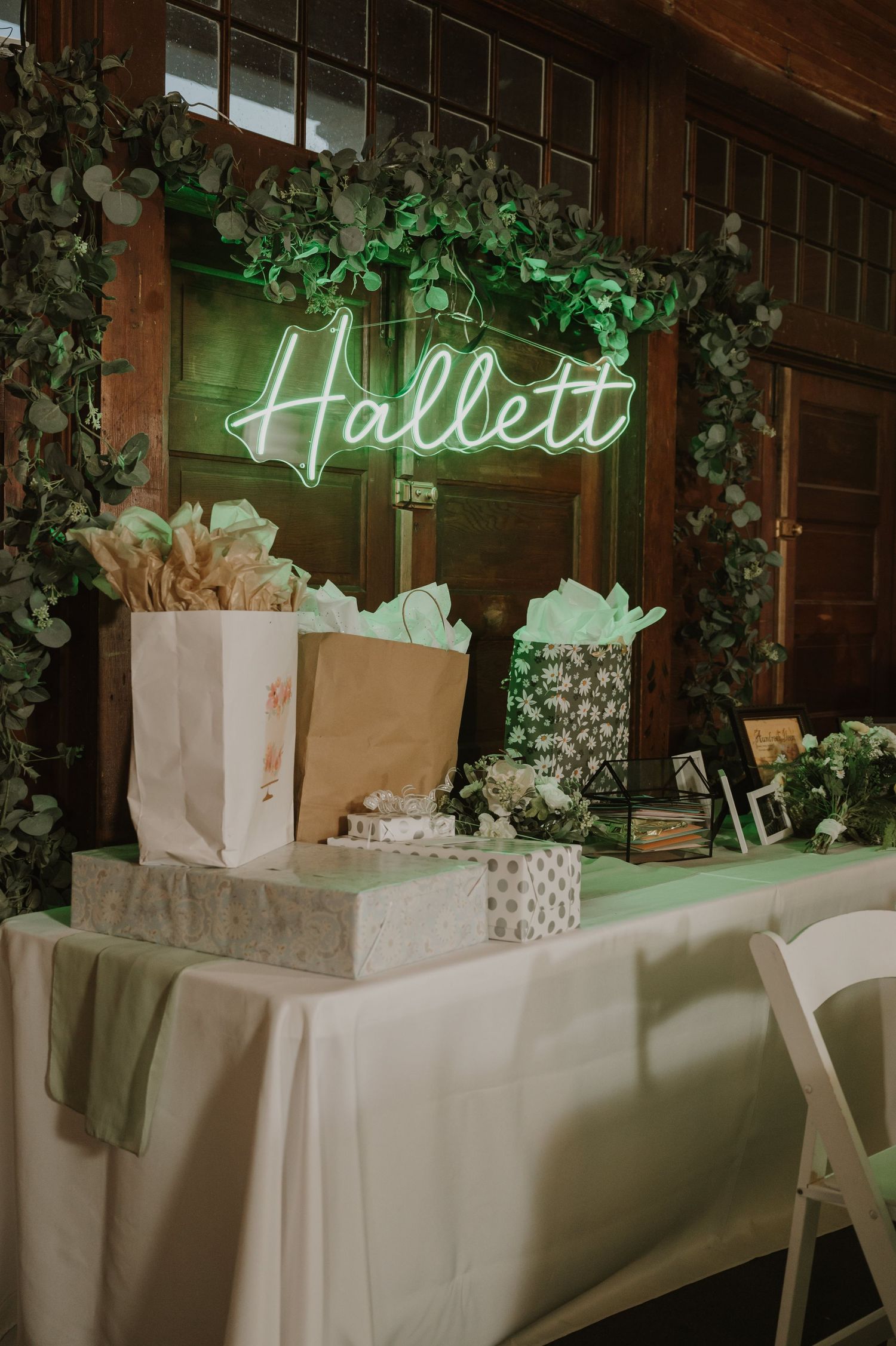 Wedding gift table decorated with greenery and neon signage against a wooden wall.
