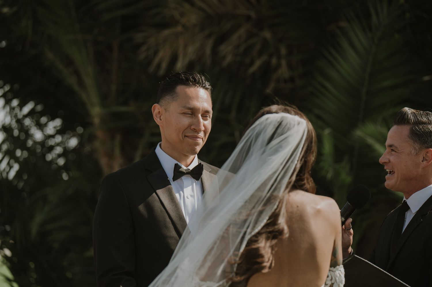 Intimate wedding ceremony moment captured in natural light under tropical foliage.