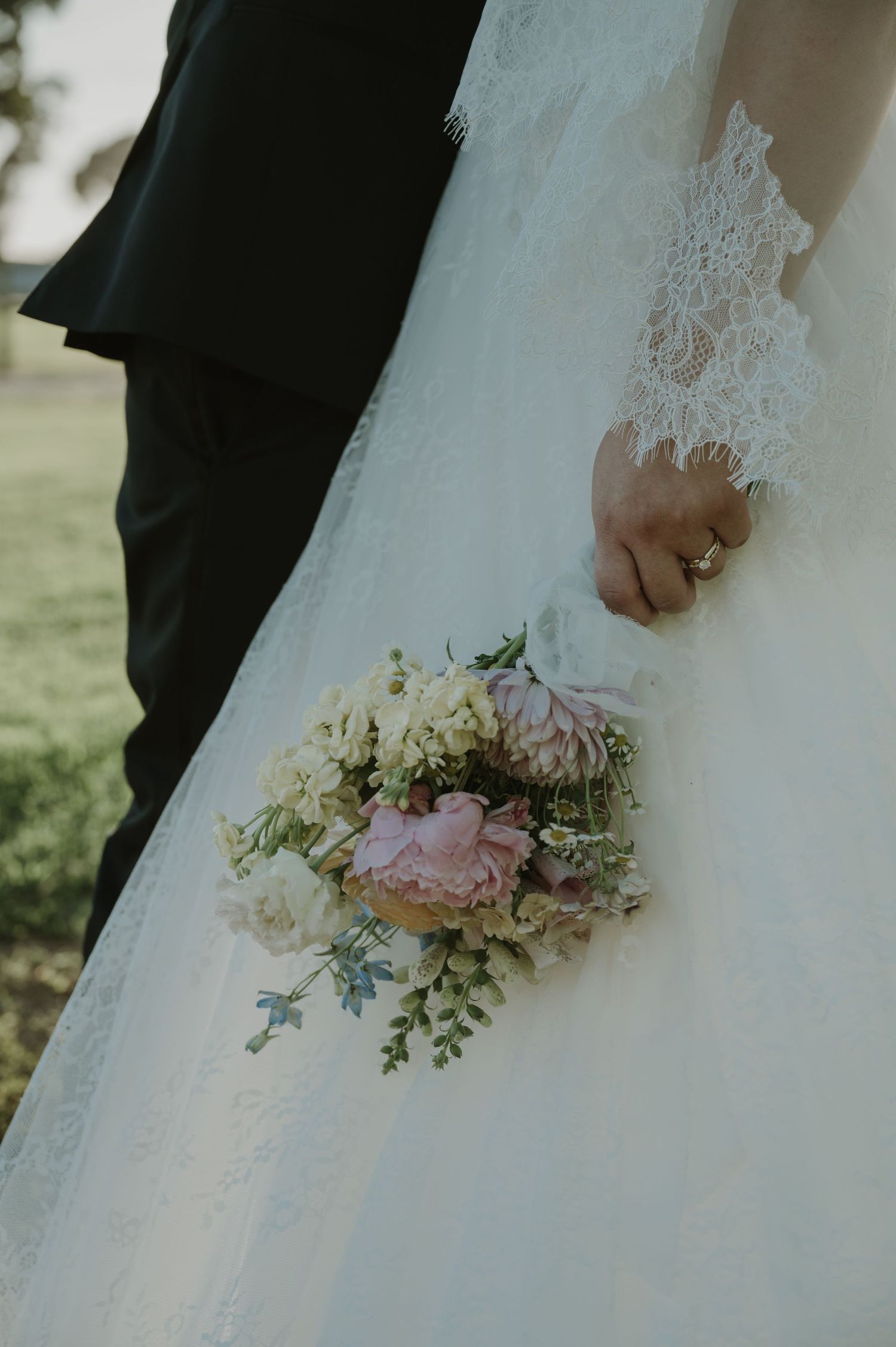 Bride holding a delicate pink and white bouquet in a lace wedding gown.