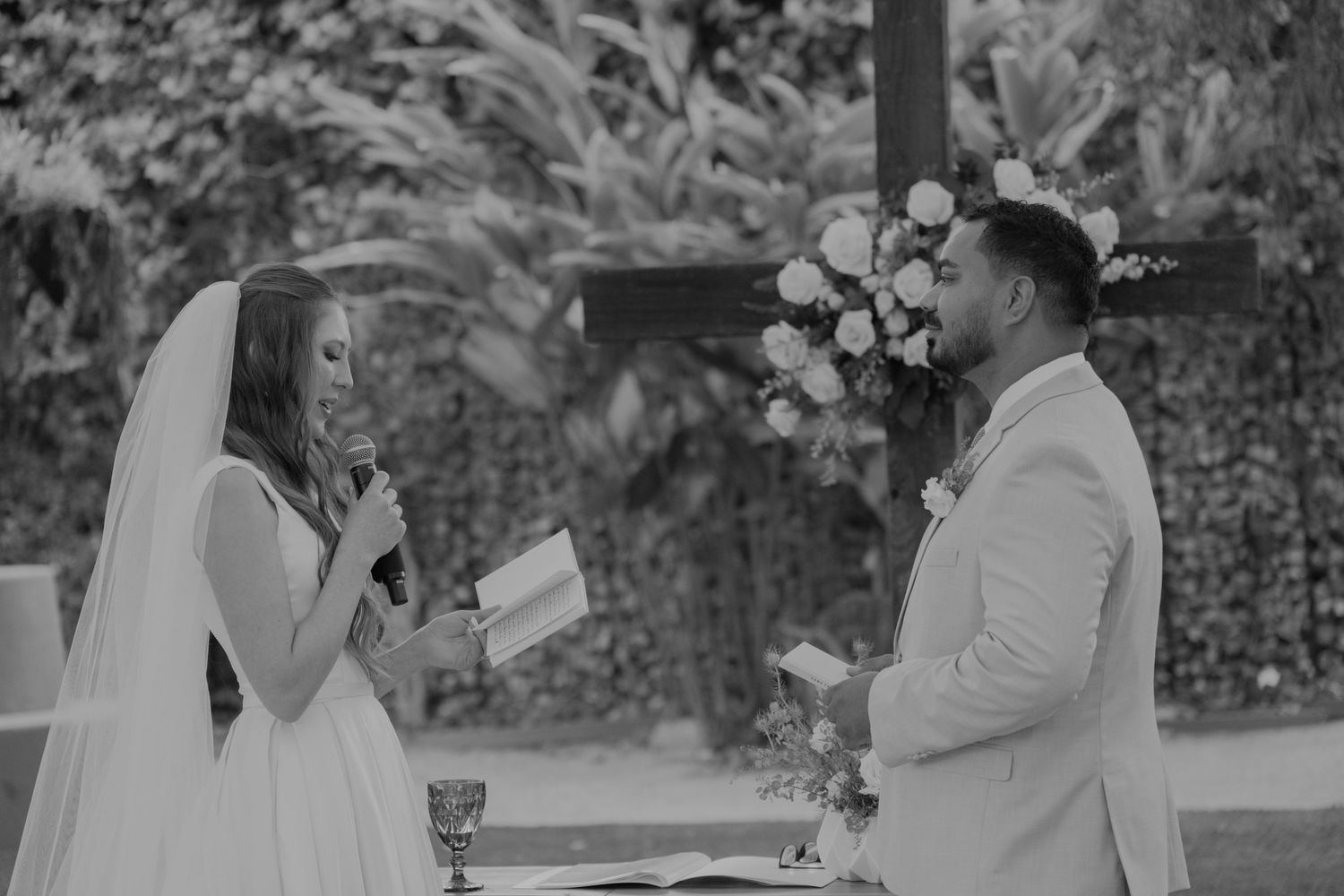 Bride and groom exchange heartfelt vows at outdoor wedding altar adorned with floral arch in black and white photo.