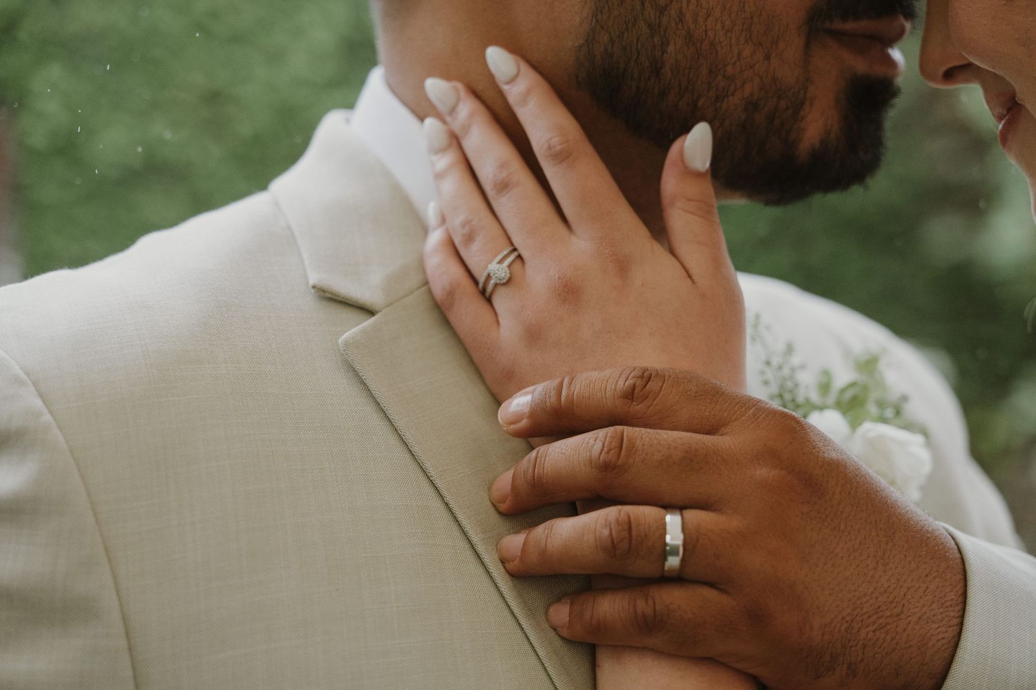 Close-up of bride's hand on groom's shoulder showcasing engagement ring and wedding bands.