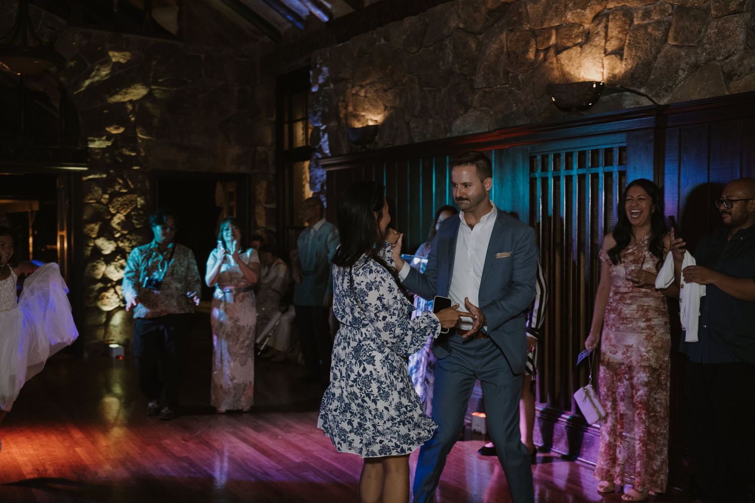Guests dancing and celebrating inside a rustic stone venue with colorful lighting at a wedding reception.
