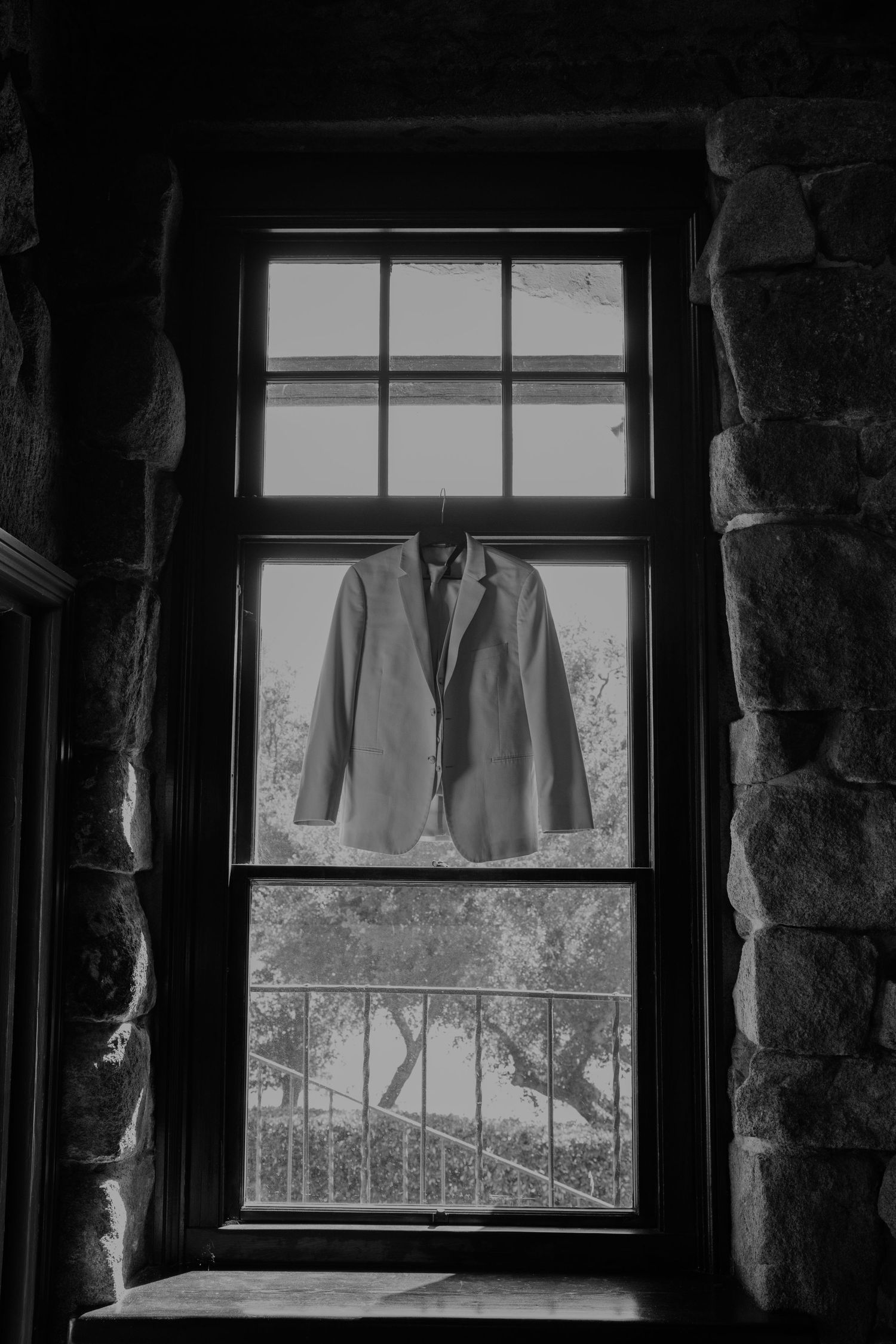 Black and white photo of a suit jacket hanging on a window frame in a stone building.