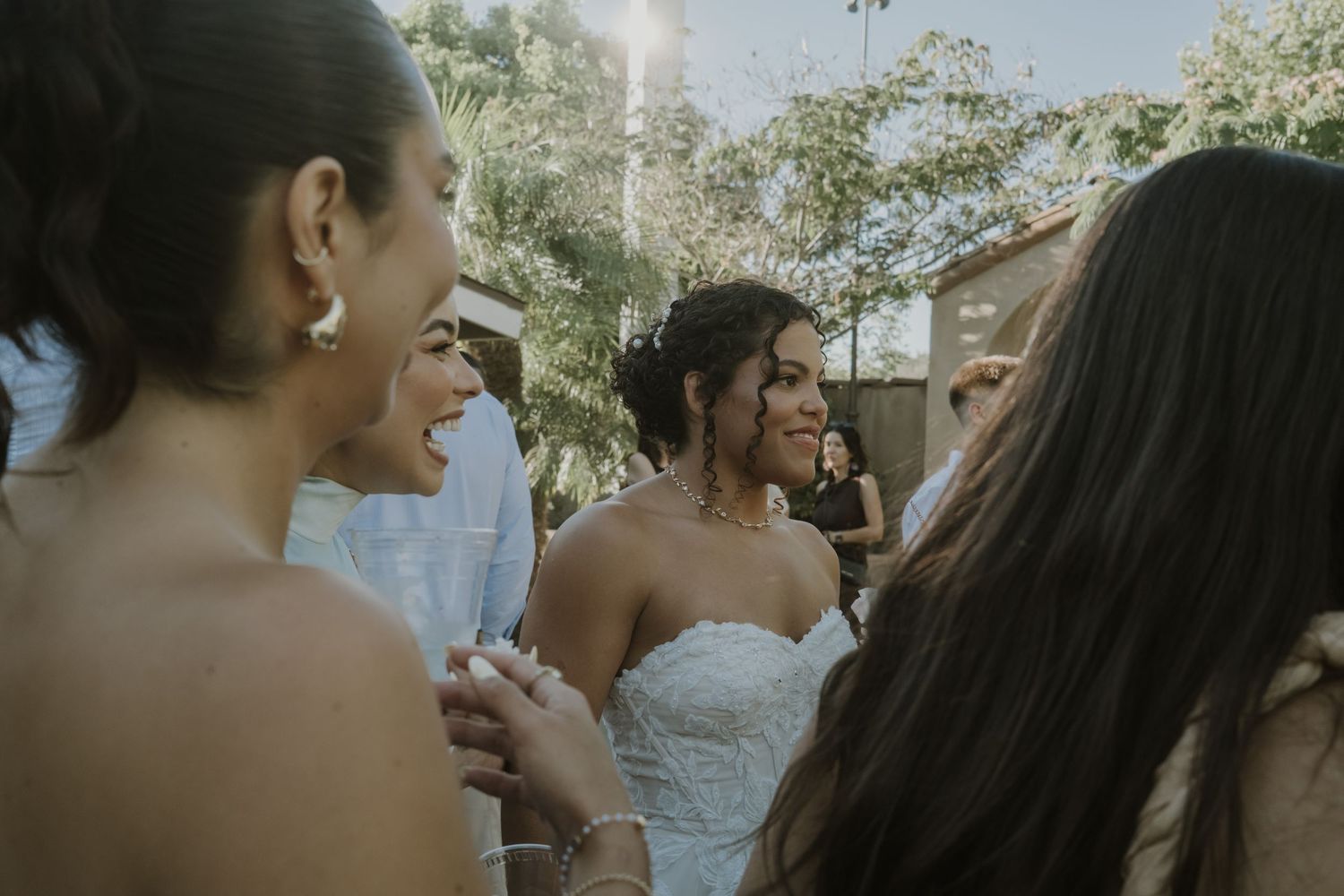 Bride in lace wedding dress smiling and celebrating with guests at outdoor wedding.