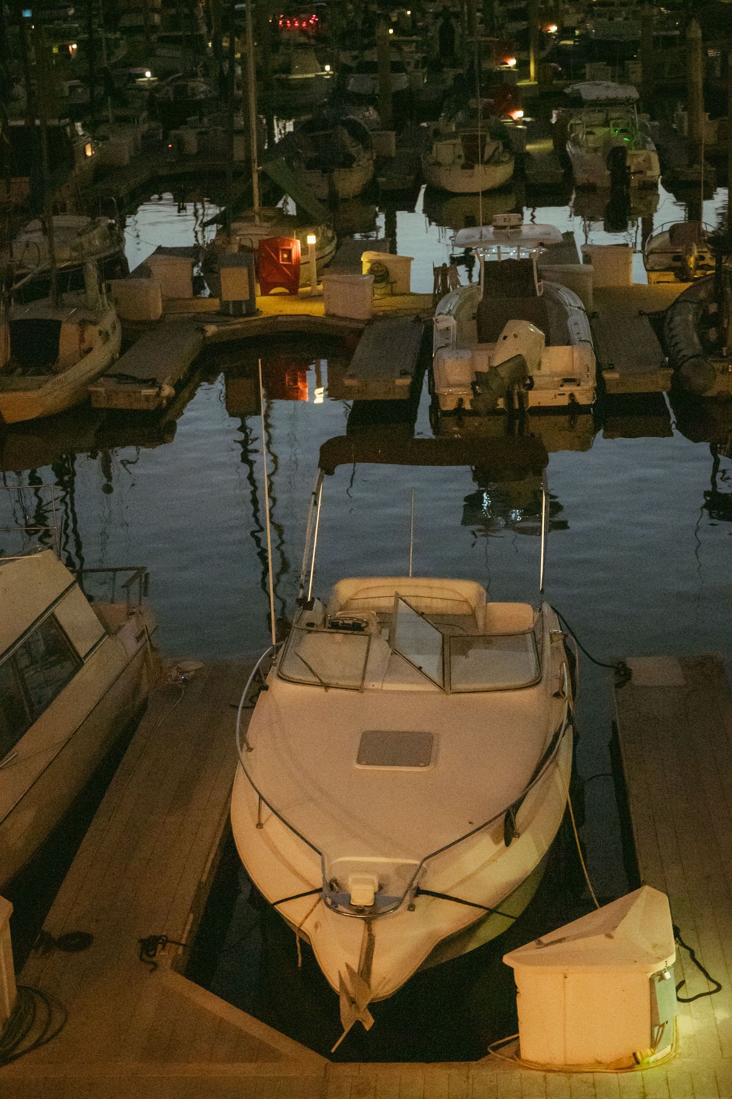 White motorboats docked at a marina at night with calm reflective water and dock lights.