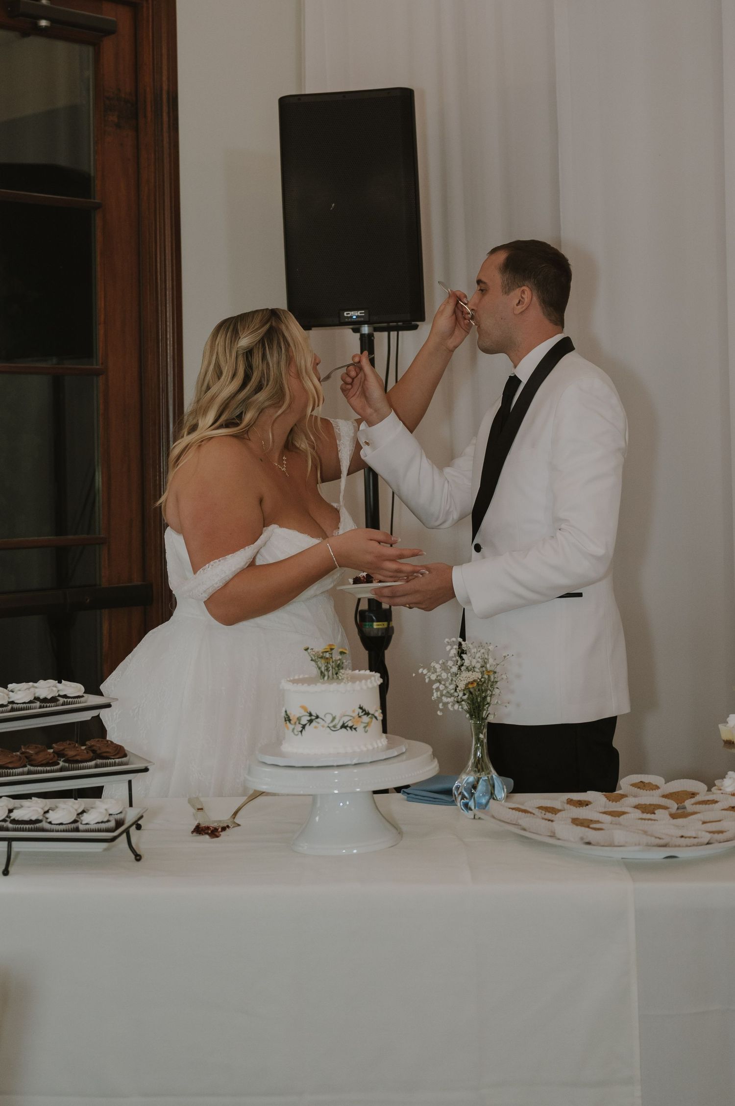 Bride and groom sharing cake cutting moment at wedding reception dessert table.