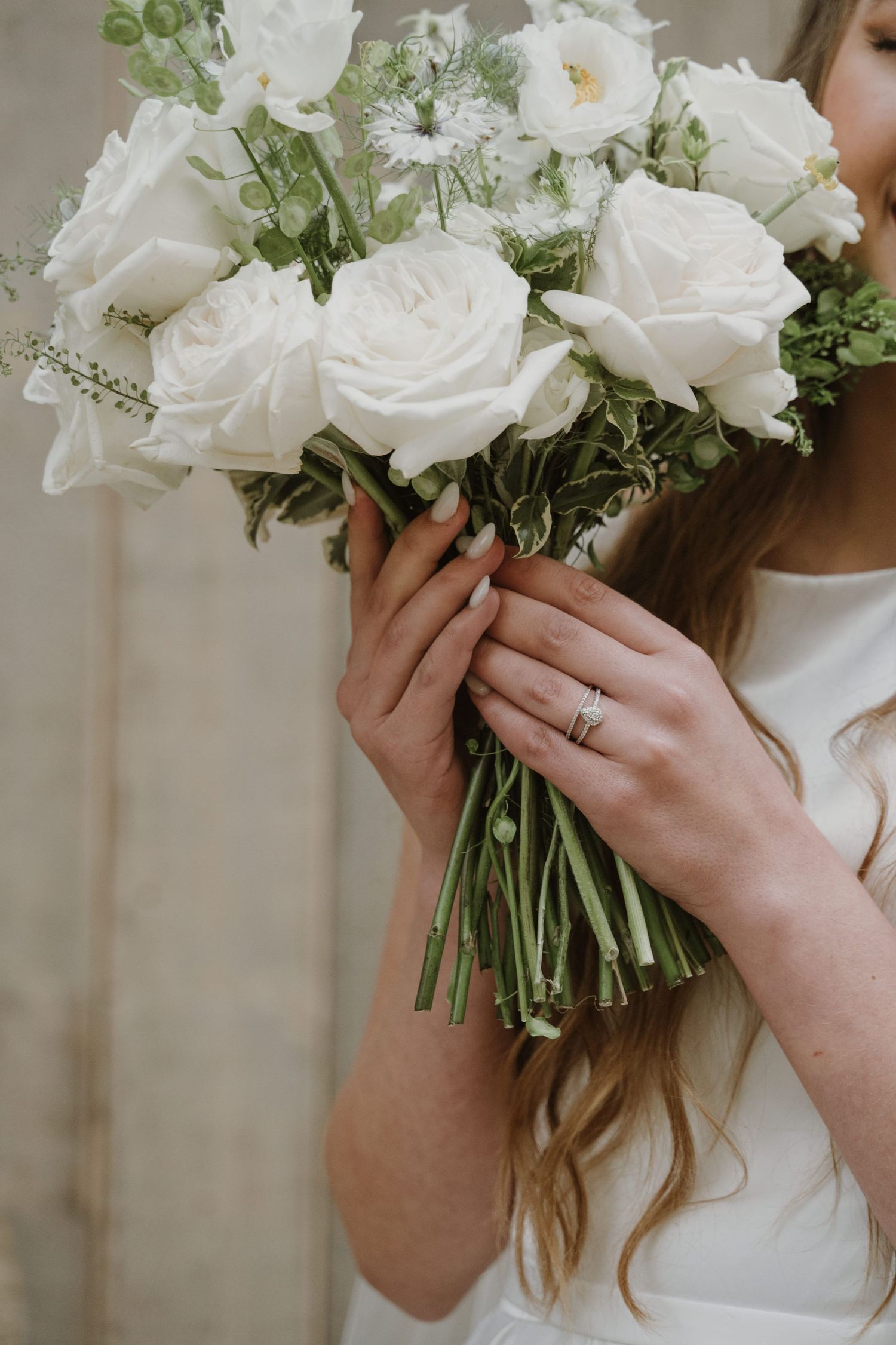 Bride holding white rose wedding bouquet with diamond engagement ring on her finger.