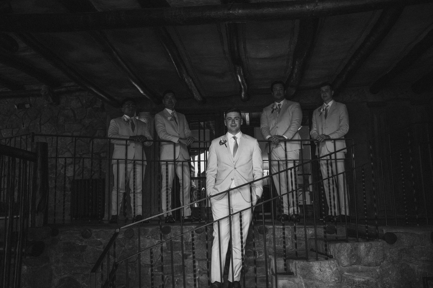 Black and white photo of a man in white suit on stairs with four men standing on balcony behind him.