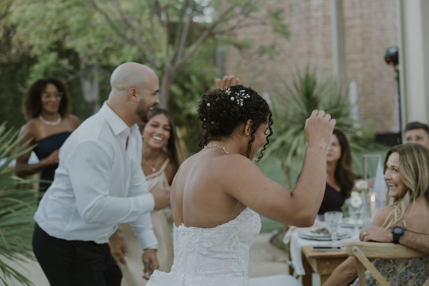 Bride and groom dancing together at outdoor wedding reception with smiling guests in background.