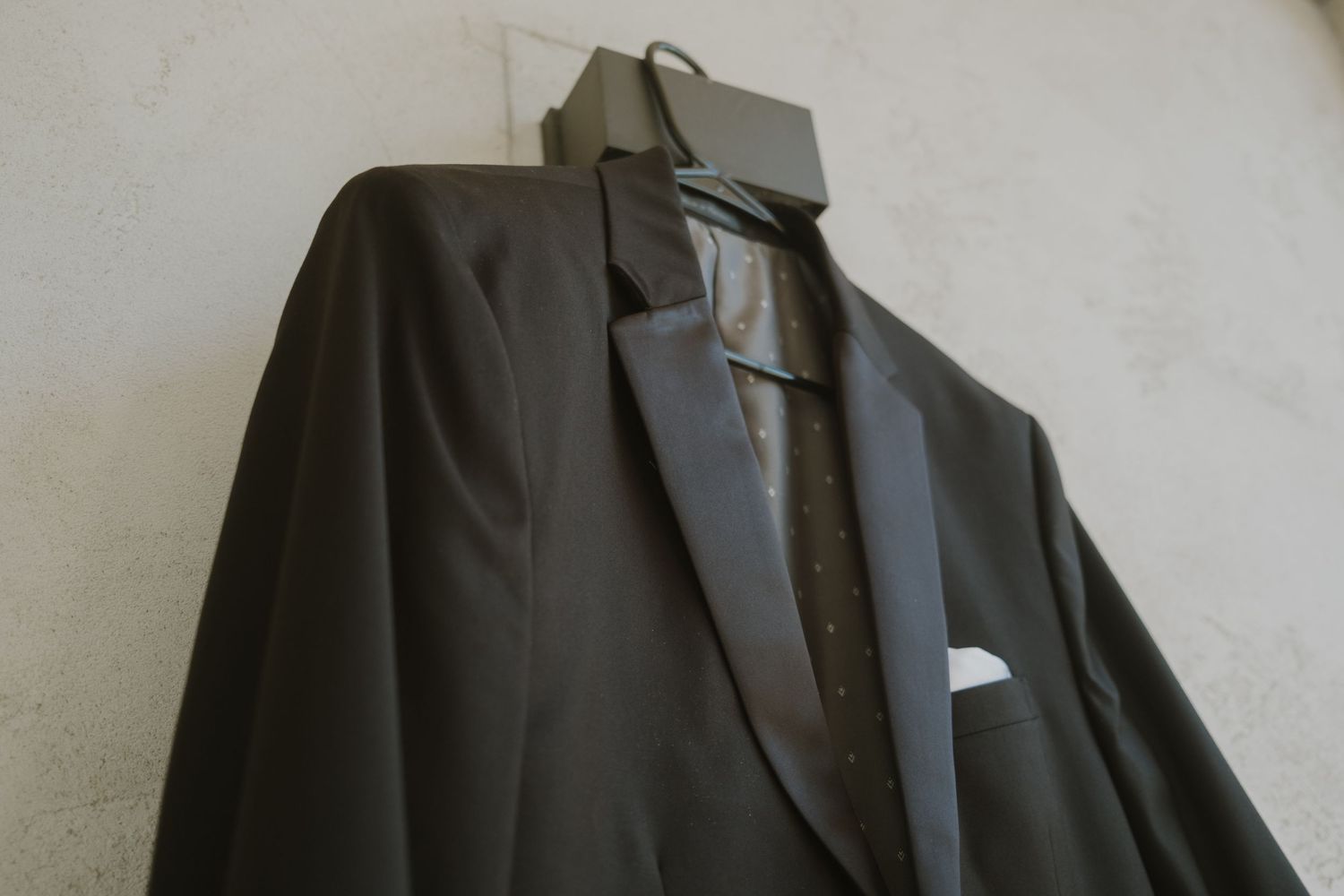 Classic black tuxedo jacket with satin lapels and white pocket square hanging on display.