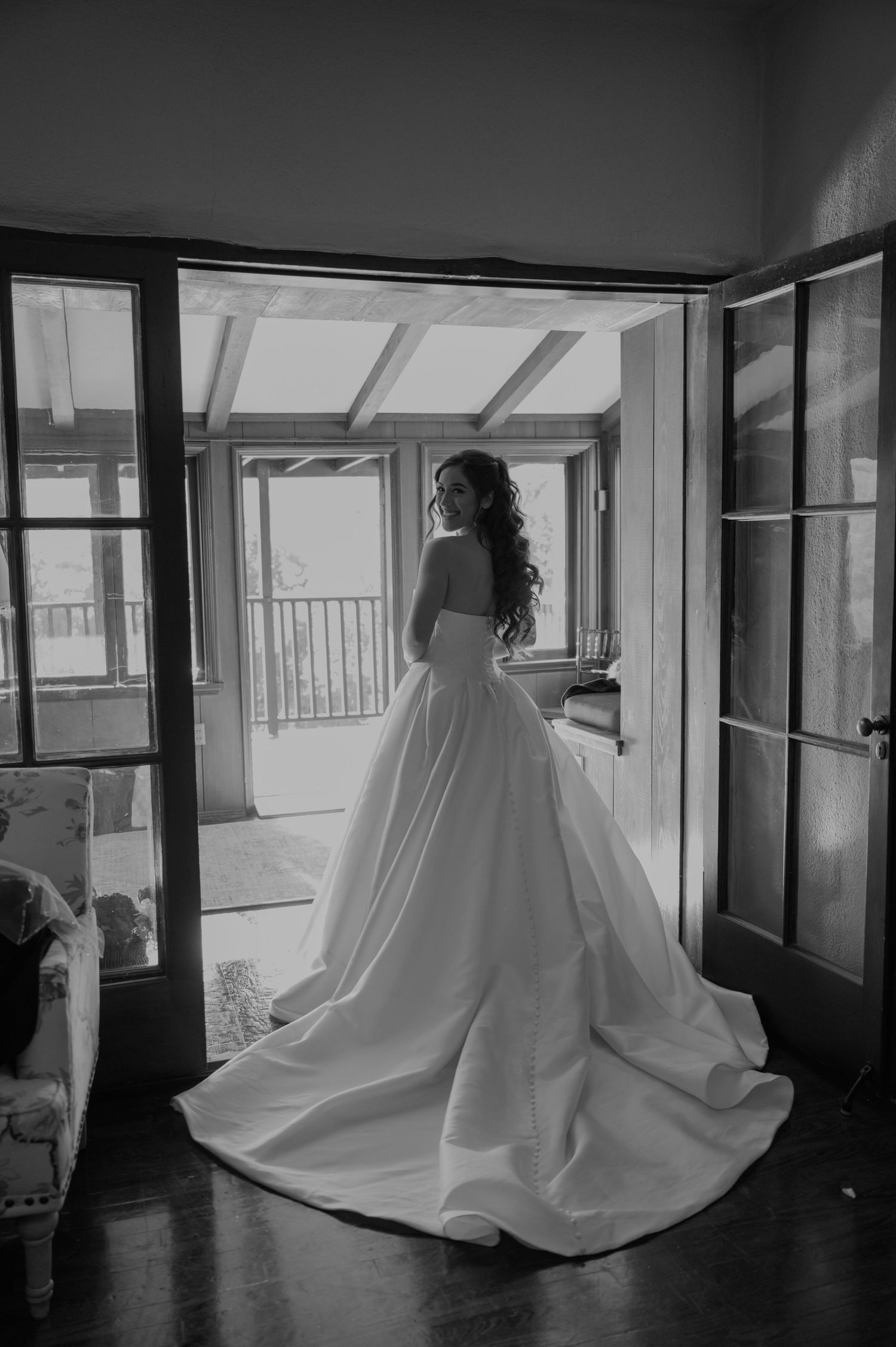 Dramatic black and white shot of flowing wedding dress train in window-lit room.