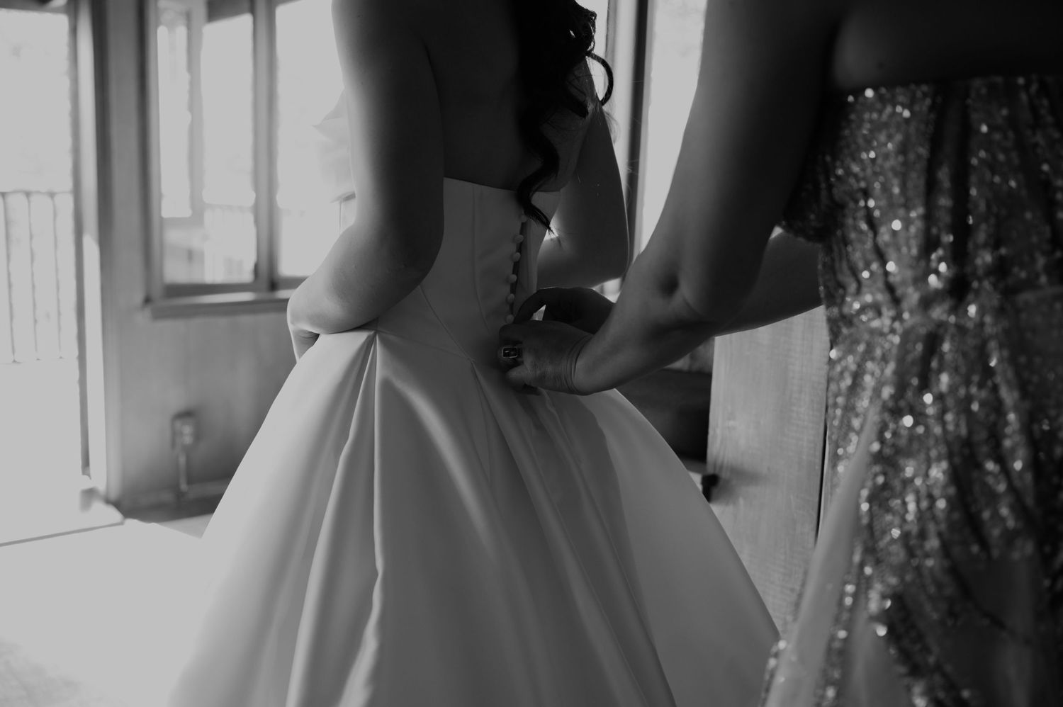 Black and white photo showing the back detail of a wedding dress being buttoned.