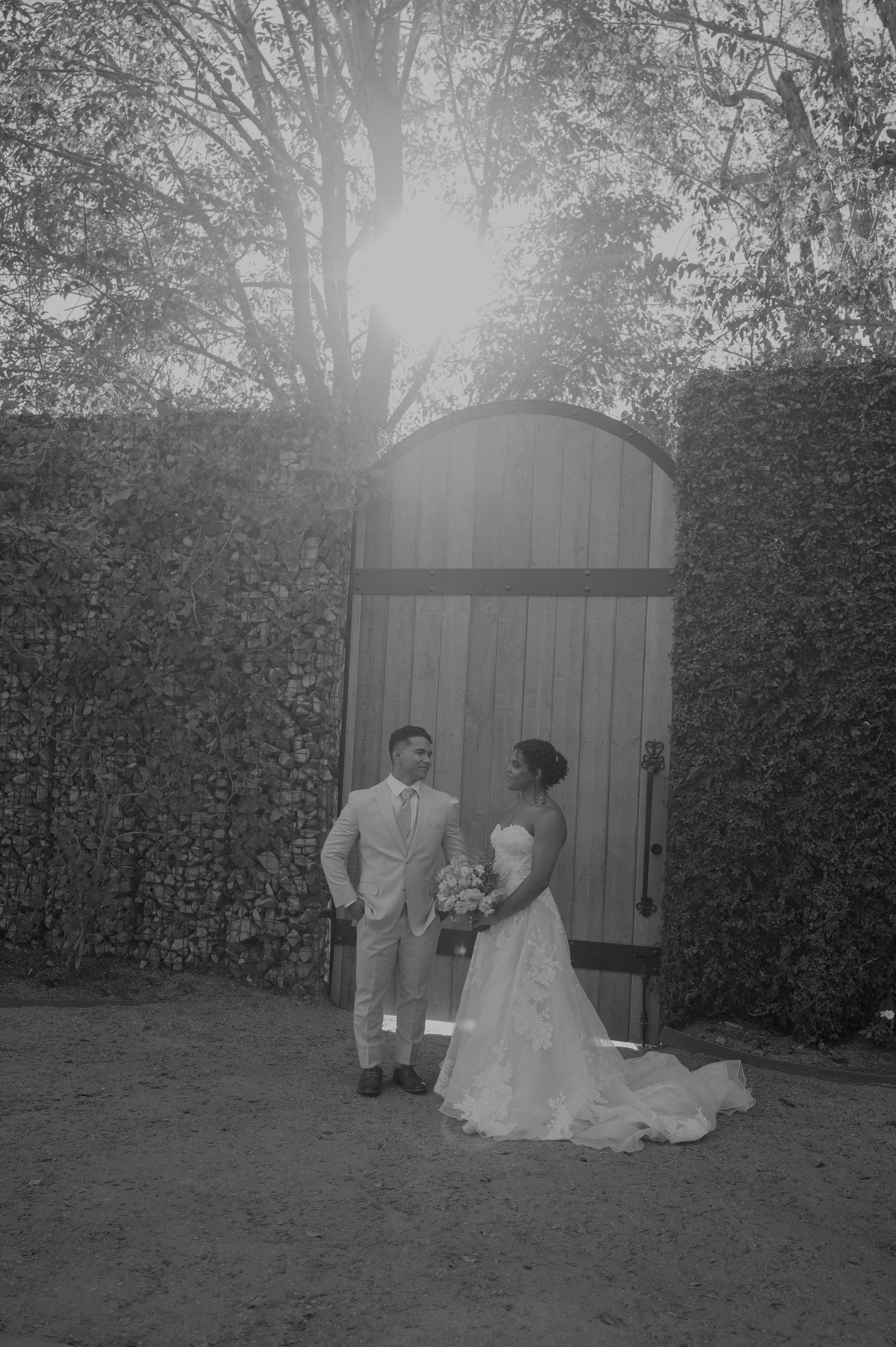 Black and white wedding photography session in a garden setting with rustic wooden gates.