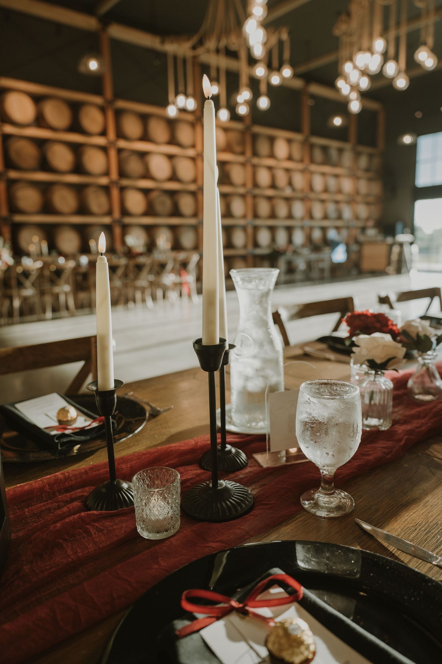 Elegant table setting with candles, glassware and burgundy runner in a rustic venue.