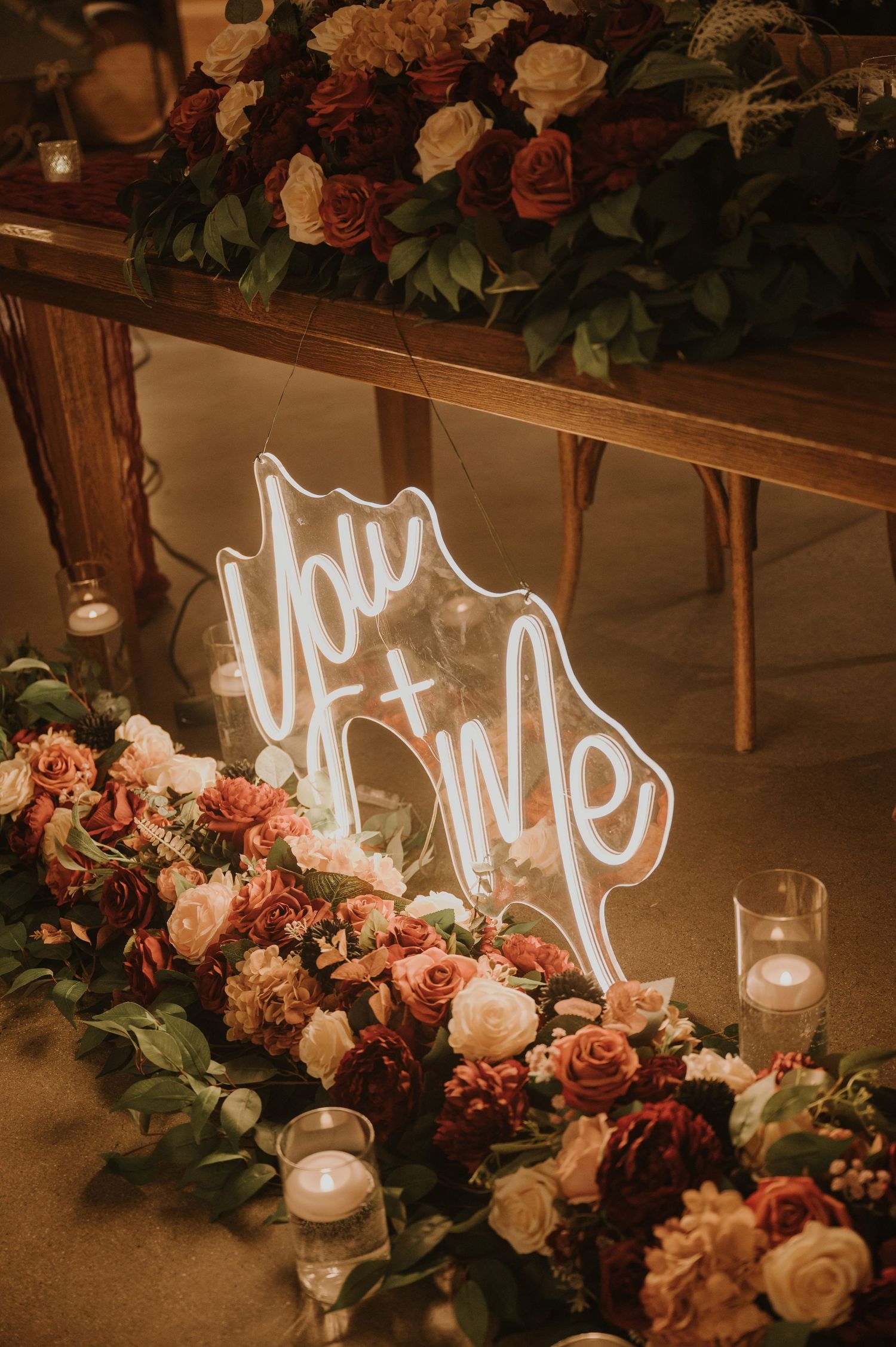Romantic floral arrangements with neon sign and candles at wedding reception.