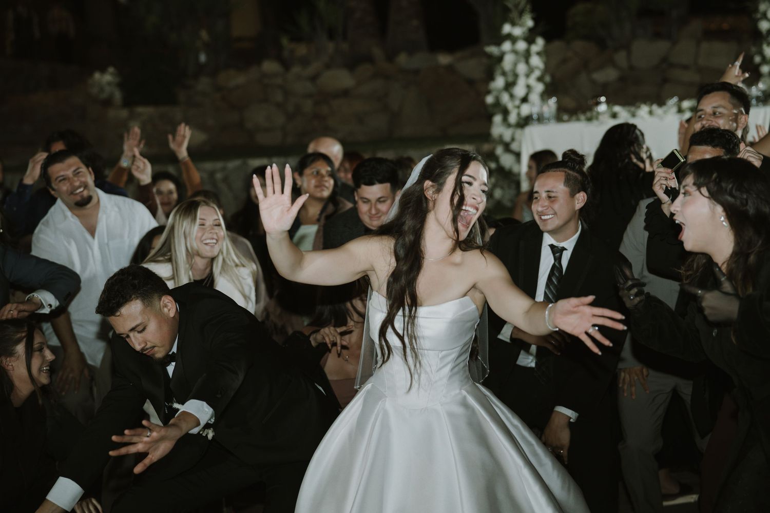 Wedding party celebrates with enthusiastic dancing in a rustic venue.