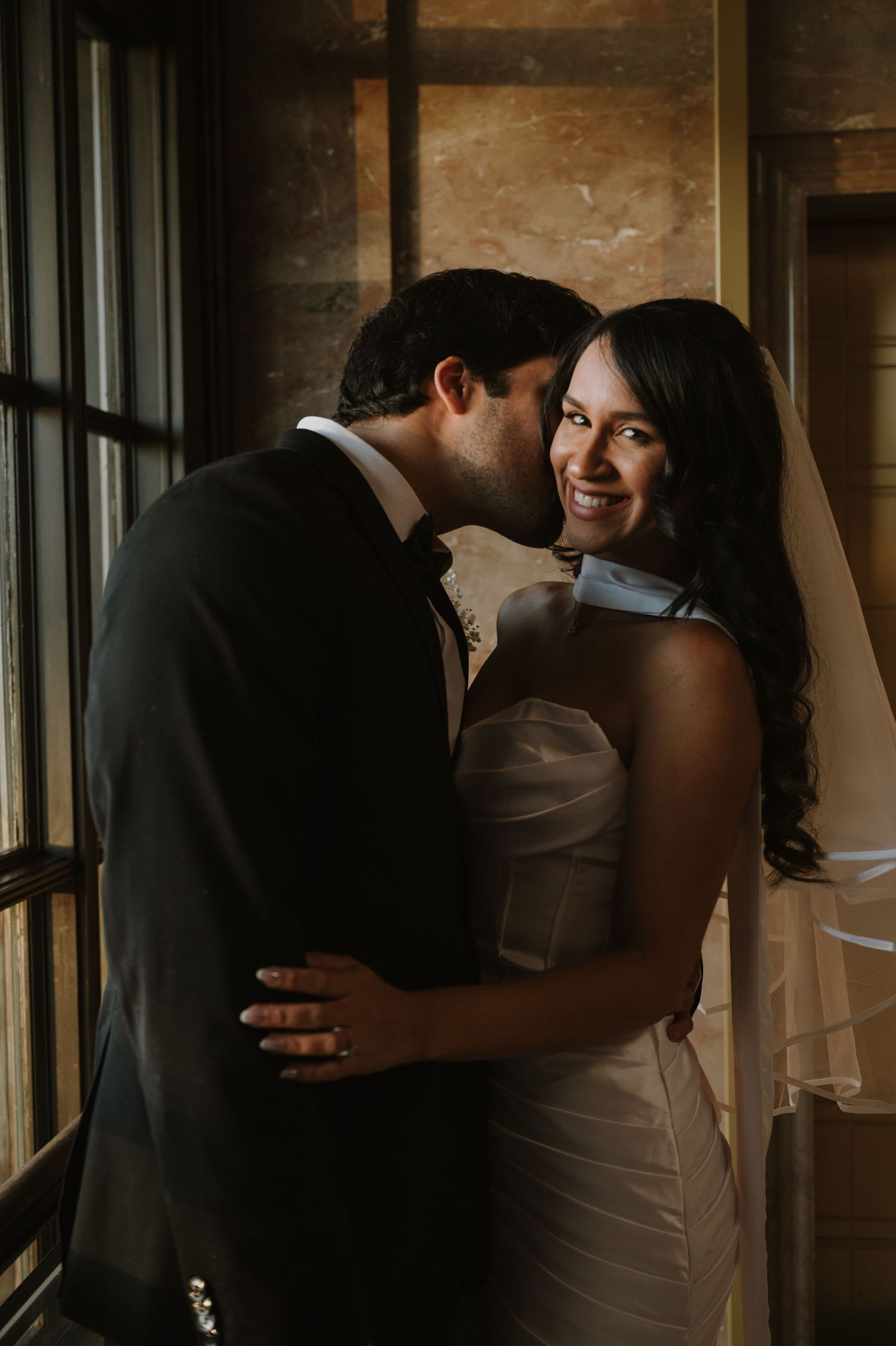 Wedding couple shares tender moments in a rustic indoor setting with natural window light.