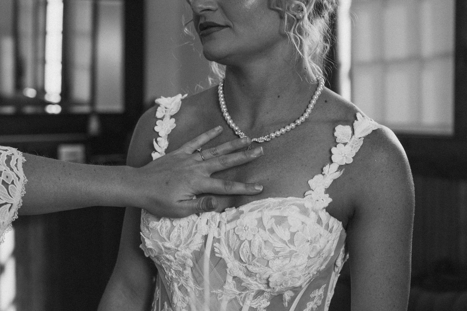 Close-up detail of a bride's pearl necklace and lace wedding dress bodice.
