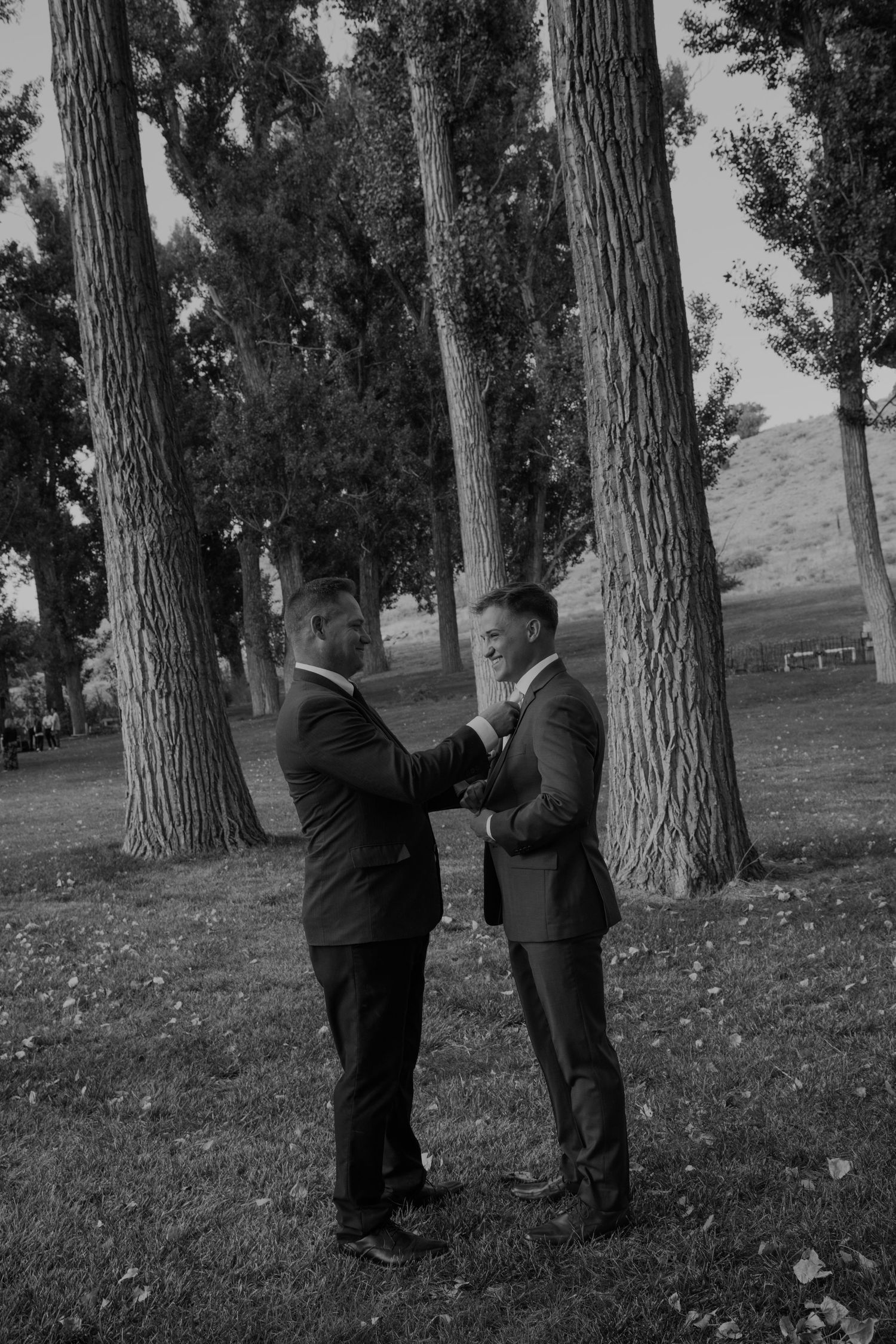 Two people in formal attire interacting playfully among trees.