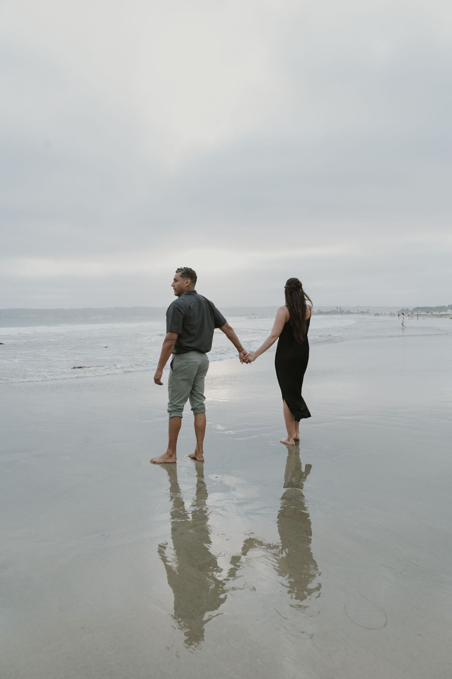 Couple holding hands while walking on reflective wet beach sand.