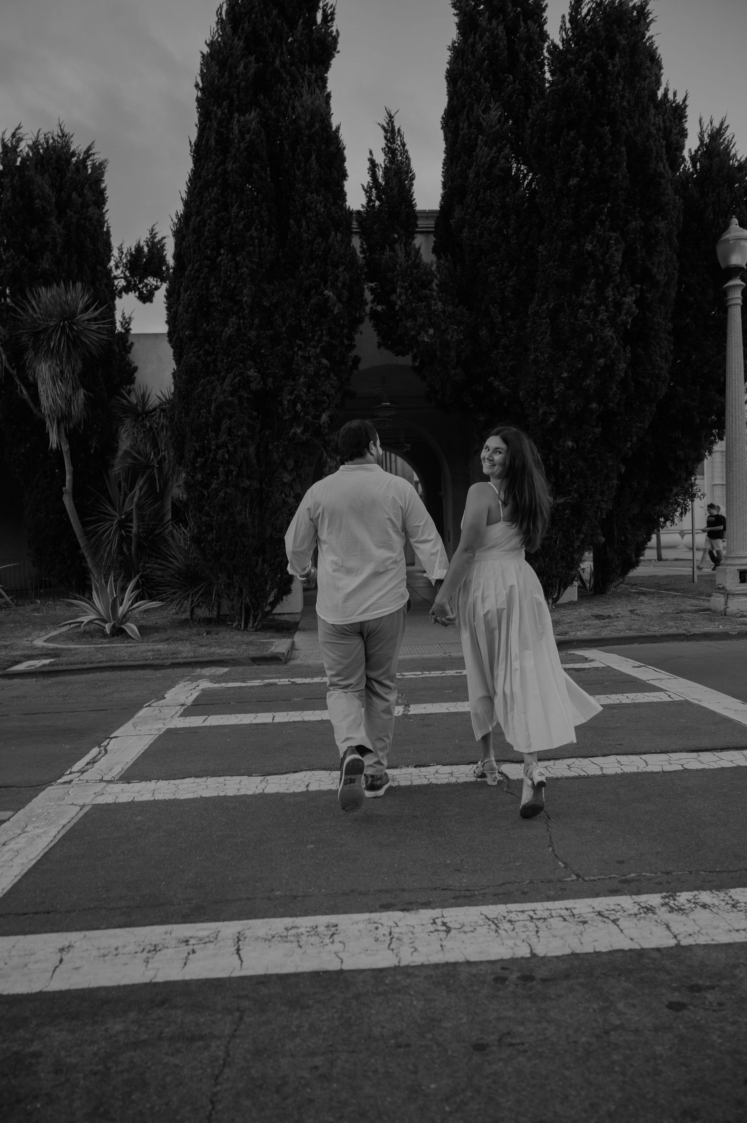 Couple walking along a path lined with tall cypress trees at dusk.