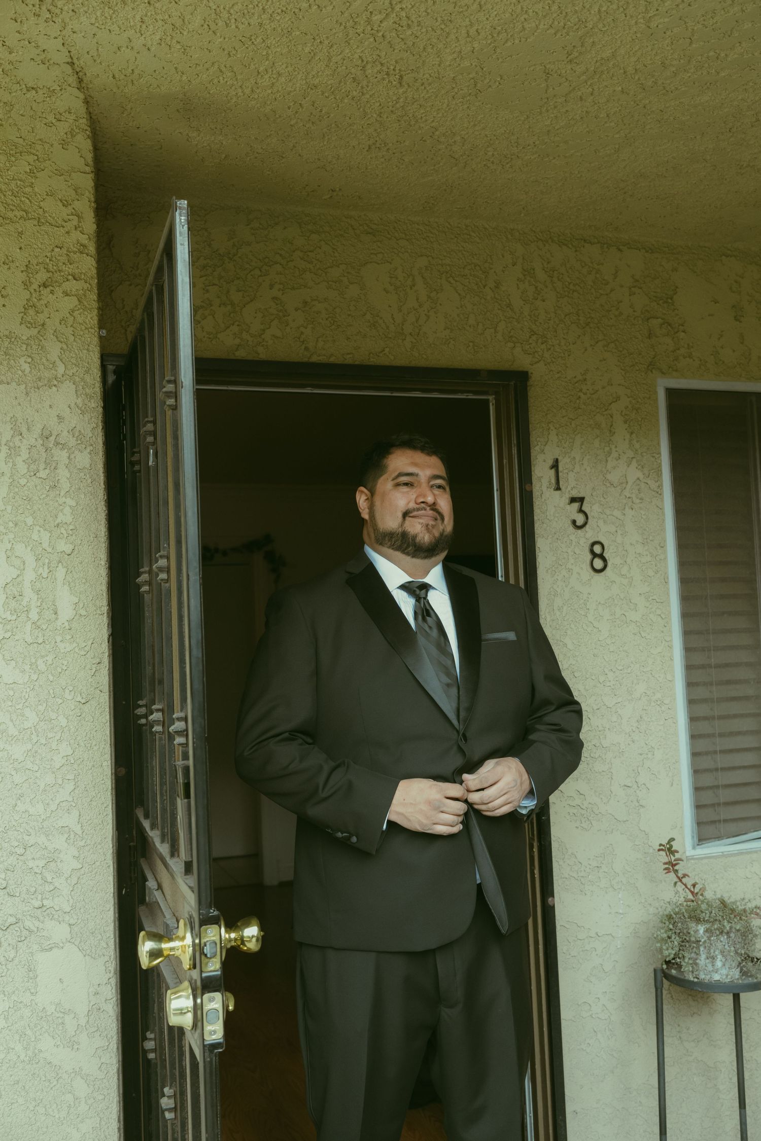 A man in a dark suit adjusting his jacket while standing in the doorway of apartment number 138.