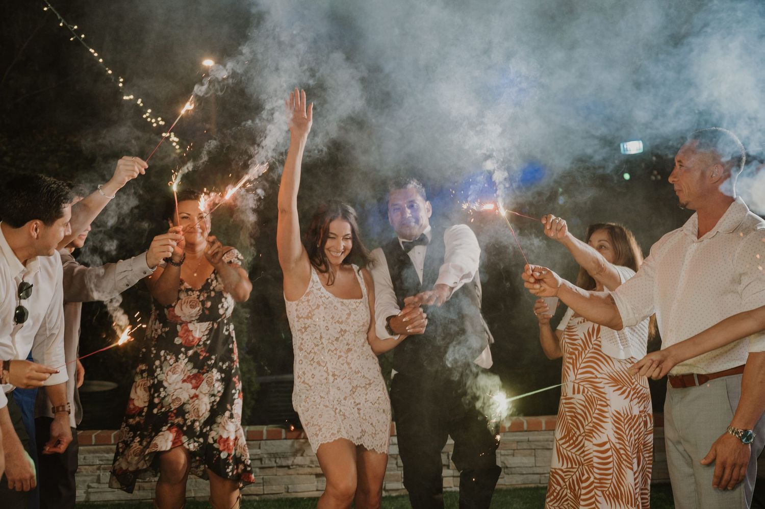 Wedding guests celebrating outdoors at night with sparklers creating a festive atmosphere.