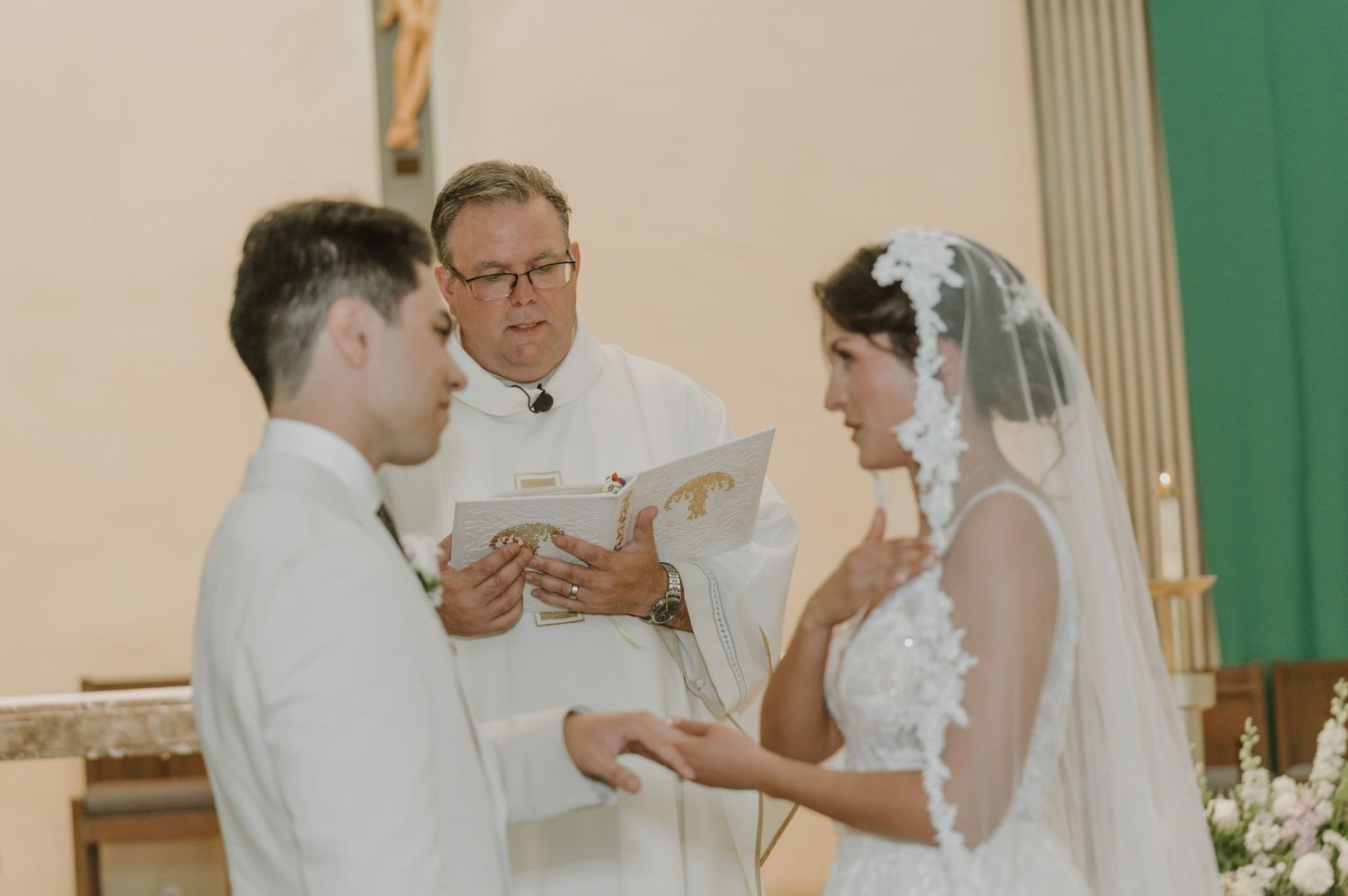 Bride and groom exchange vows before officiant reading from book during intimate church wedding.