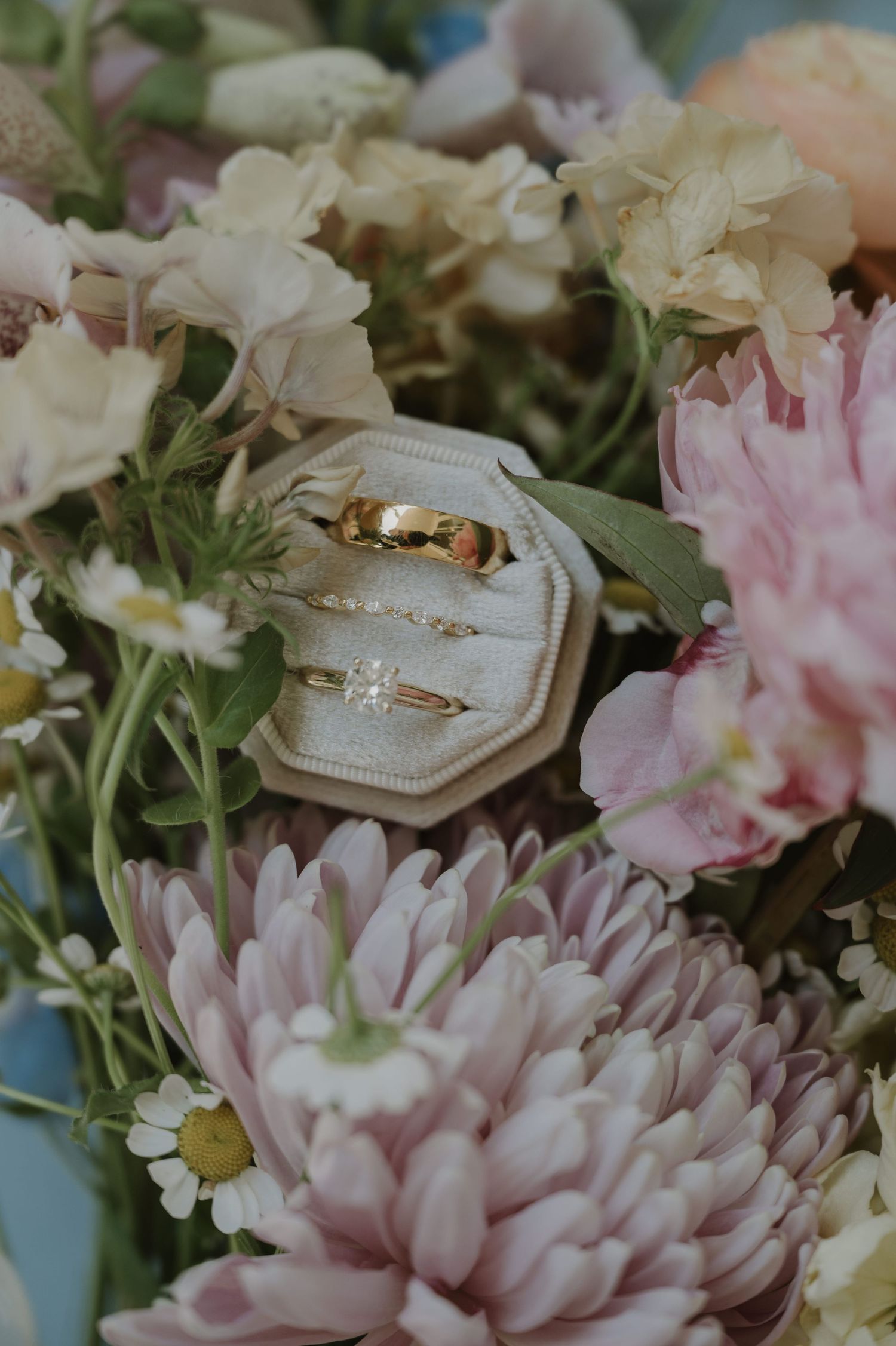 Gold wedding rings in a velvet ring box surrounded by pink and cream florals.