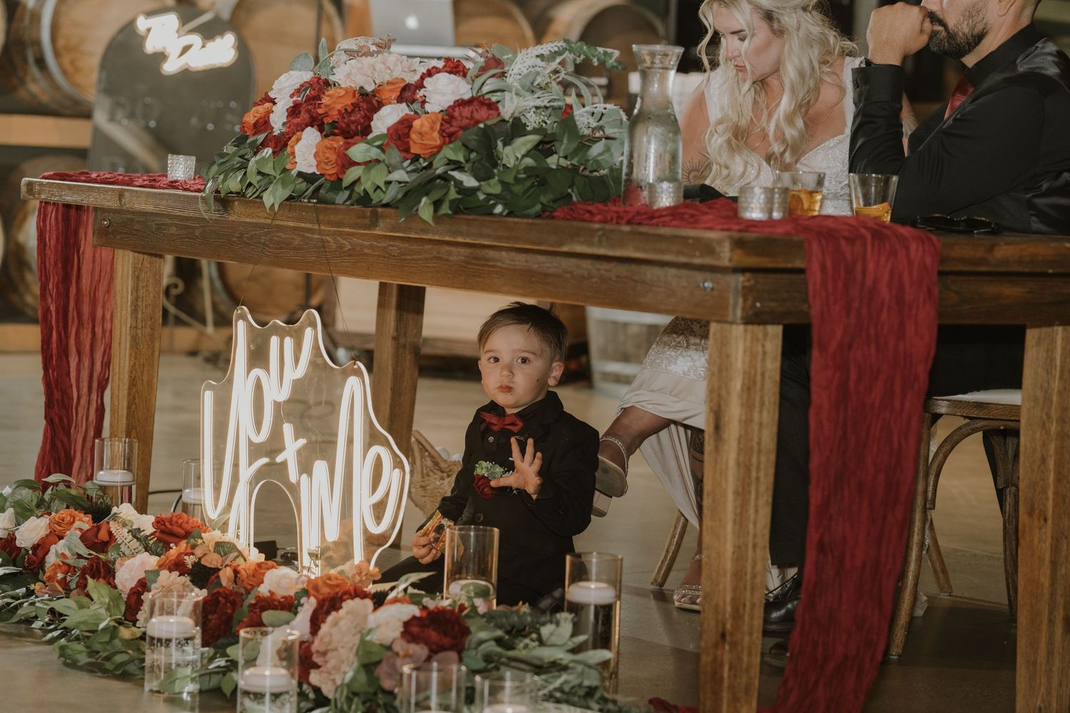 Candlelit table settings with red floral arrangements and greenery in a rustic venue.