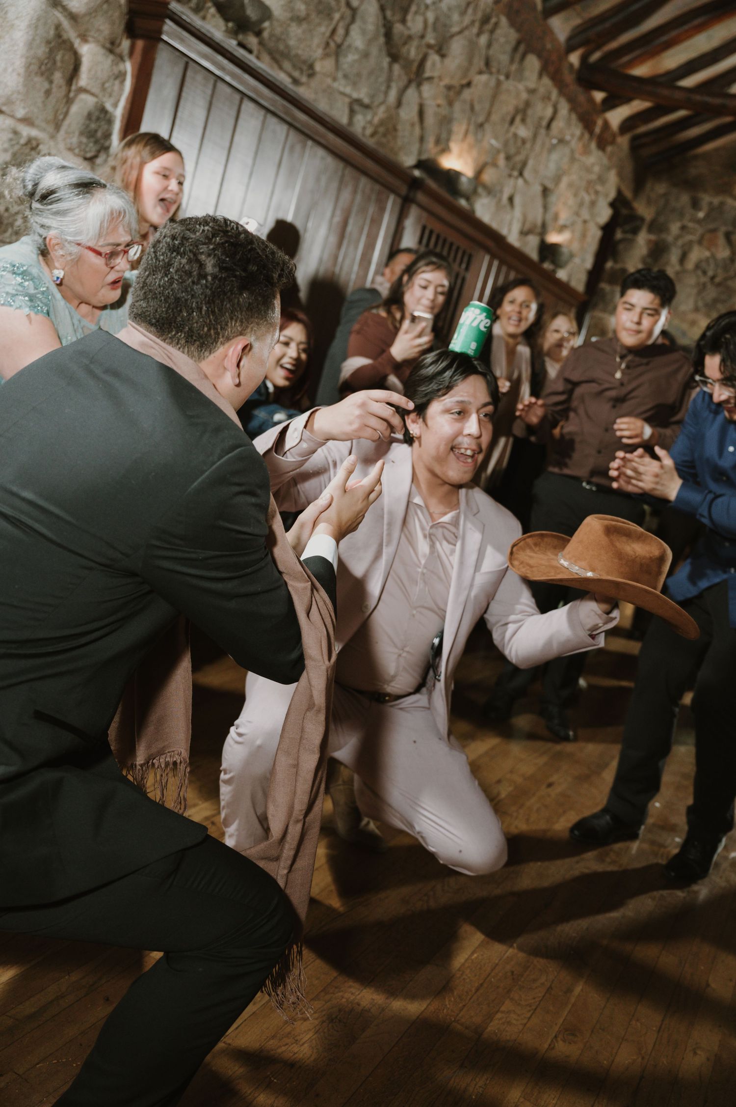 Wedding guests dance energetically on a wooden floor in a rustic stone venue.