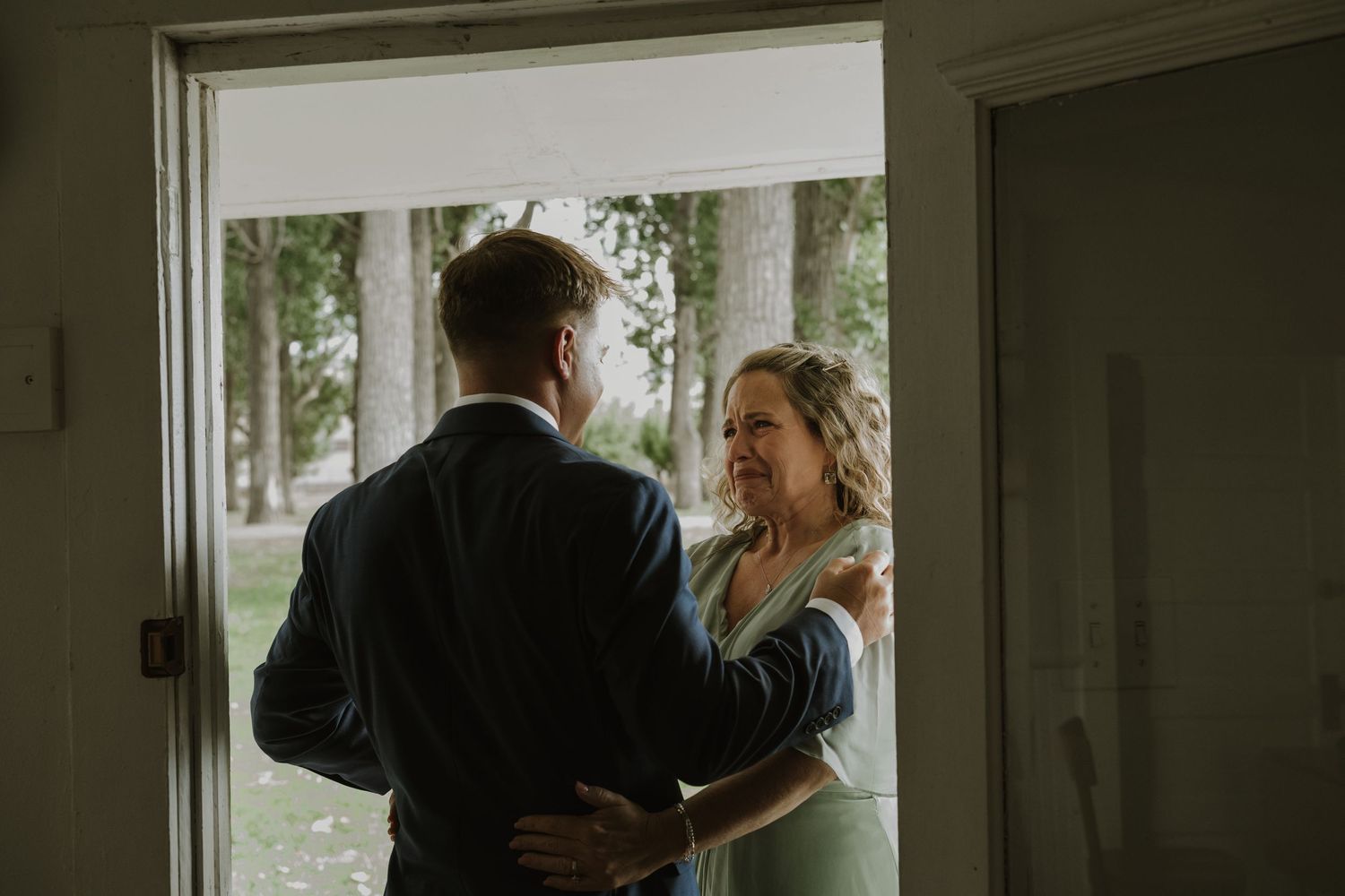 Two people share an intimate moment near a window in a dimly lit interior space.