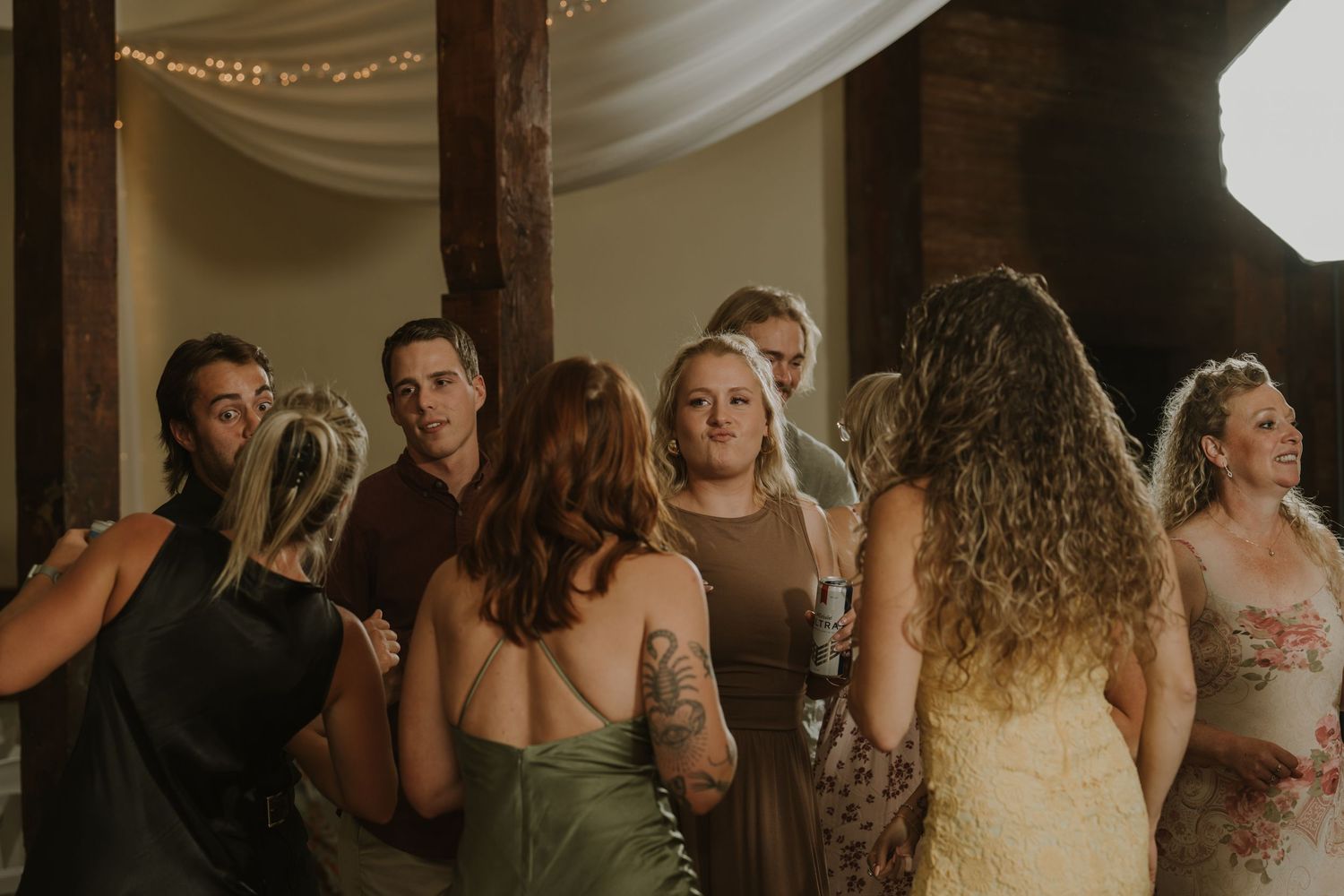 Wedding celebration with string lights and white fabric draping across wooden beams.