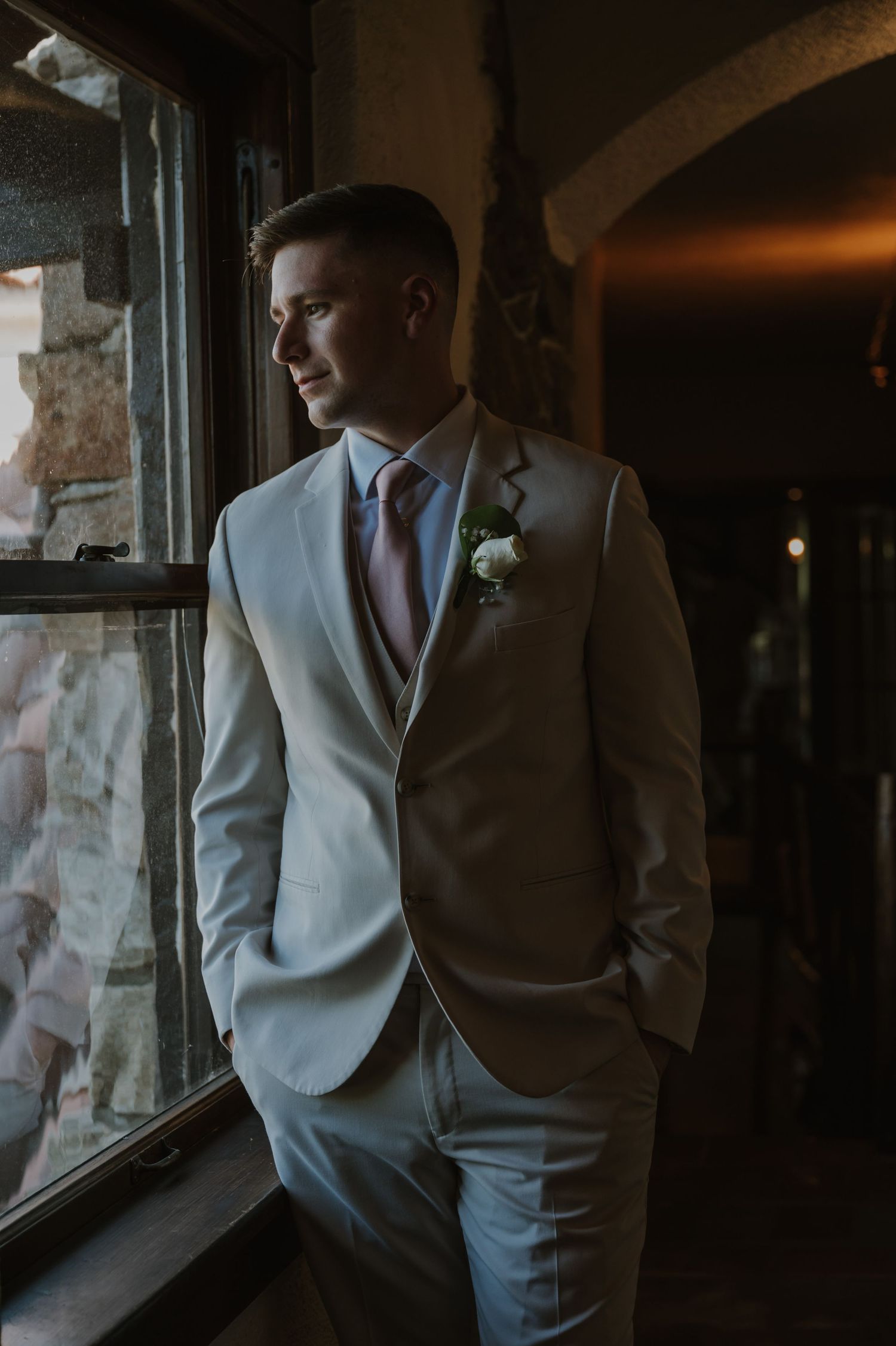 Moody portraits of person in light colored suit by window.