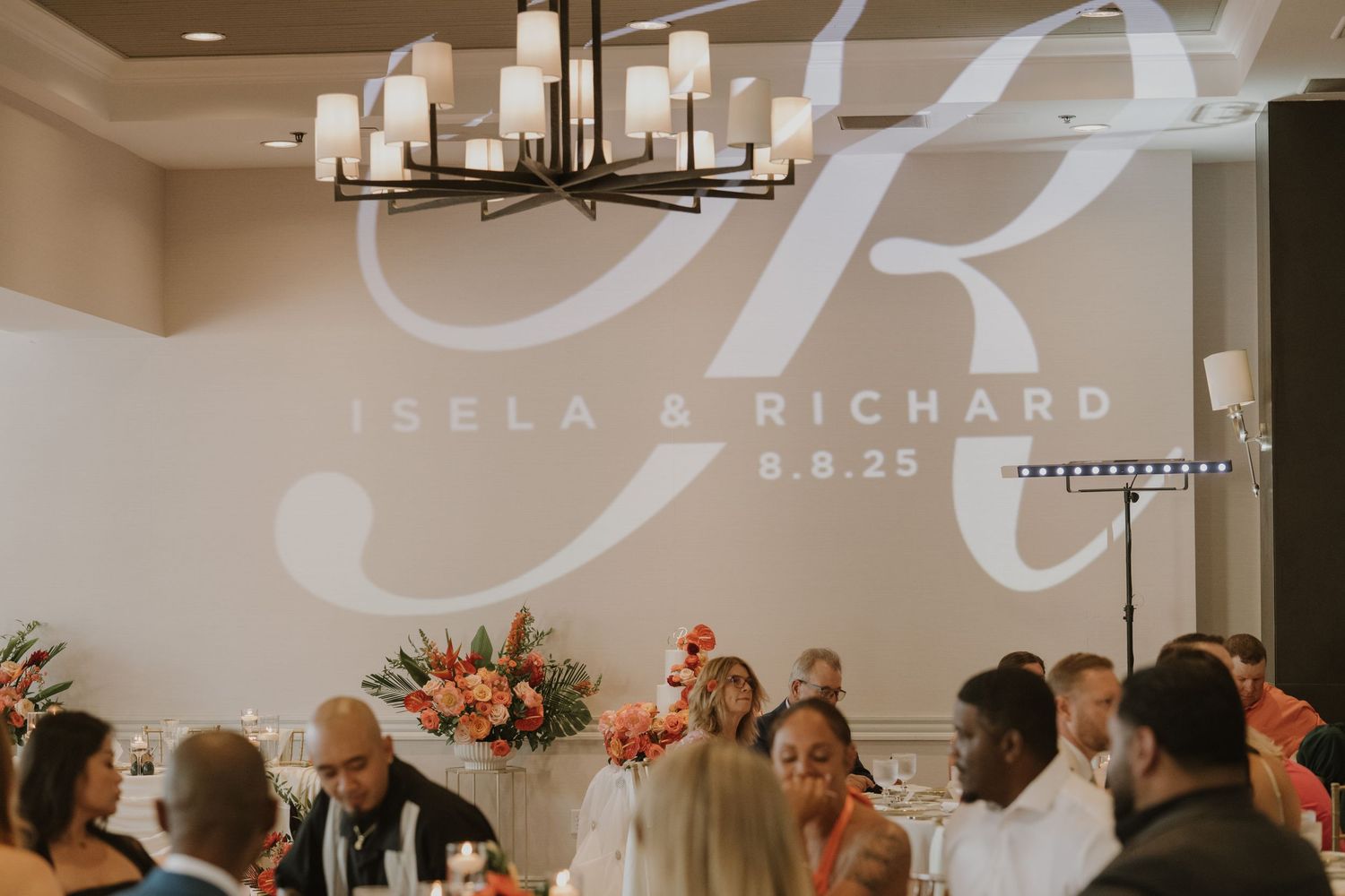 Wedding reception venue with monogram projection and coral floral decor.
