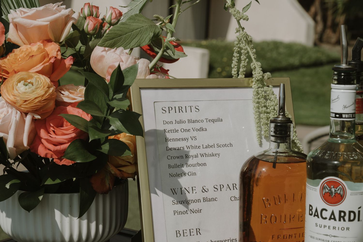 Wedding bar setup with drink menu signs and floral arrangements.