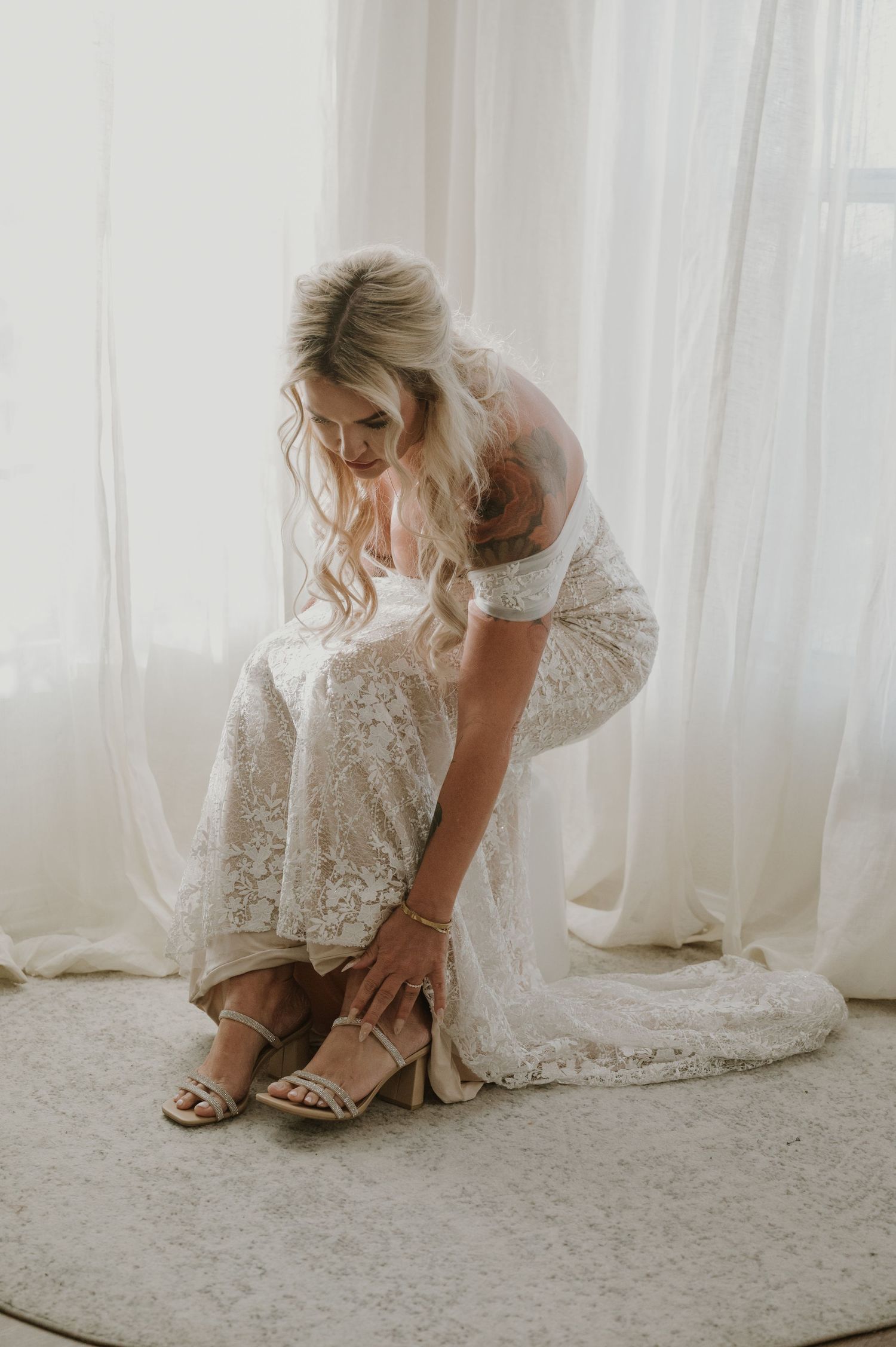 Elegant lace wedding dress and bridal preparations in a bright room with white curtains.