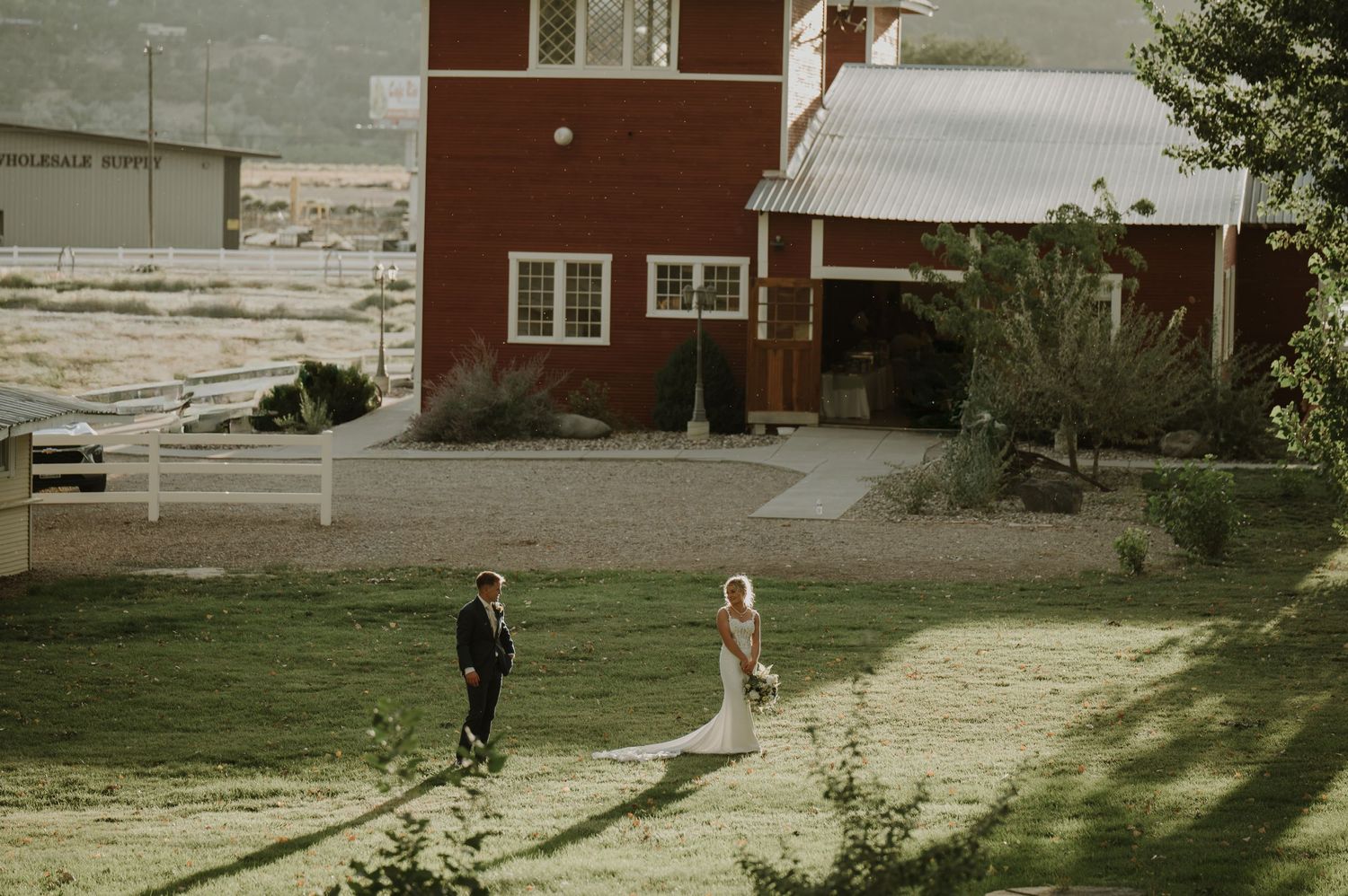 A distant view of a wedding celebration on a grassy hillside with red buildings.