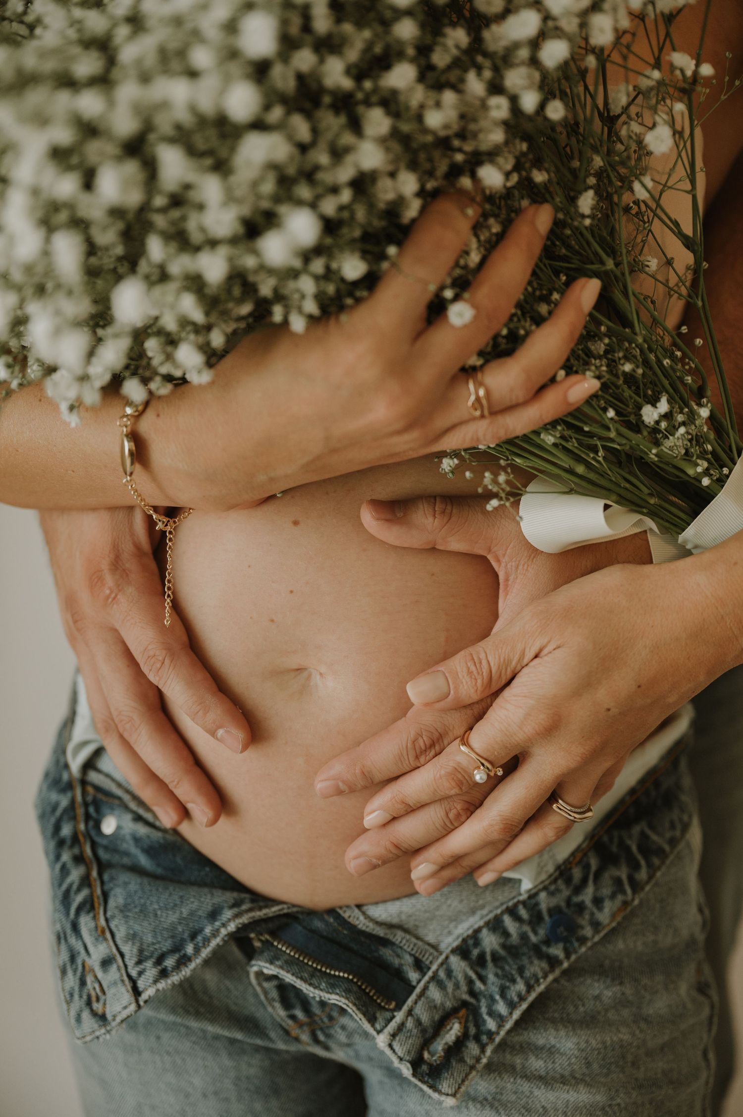 Close-up of hands cradling a pregnant belly with flowers in the background.