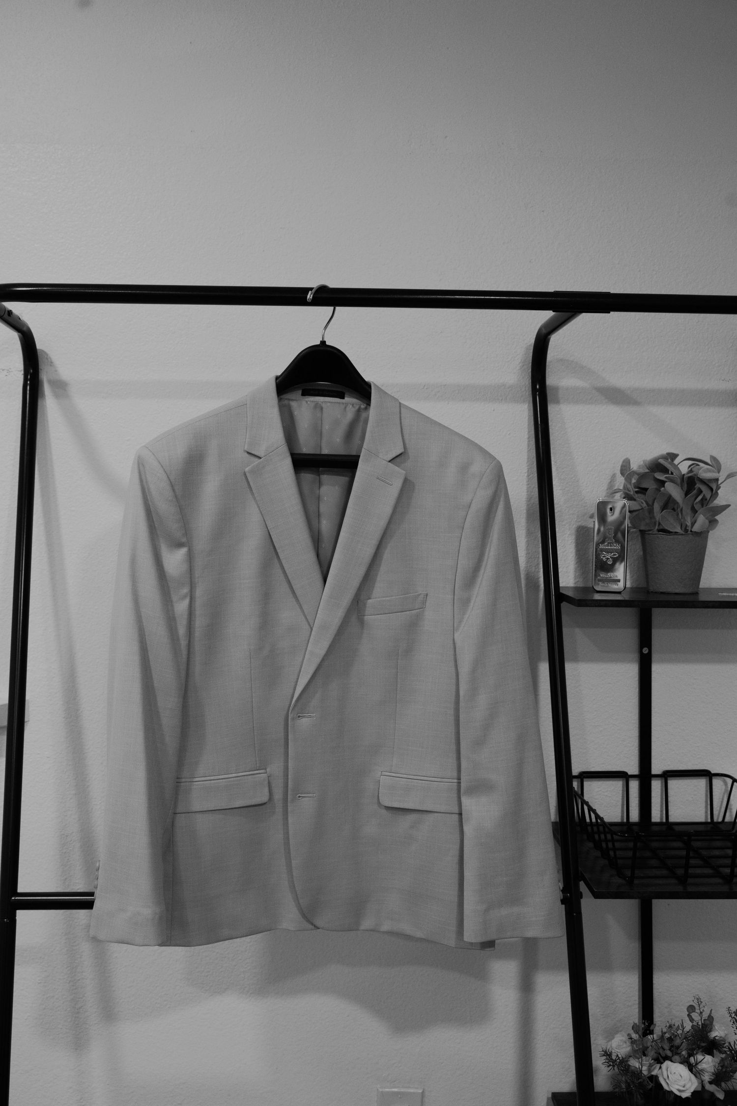A light-colored men's blazer hanging on a black hanger on a clothing rack in a minimalist room.